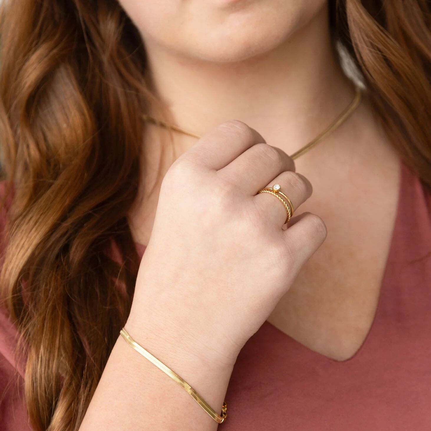 Person wearing gold jewelry including a necklace, ring, and bracelet.