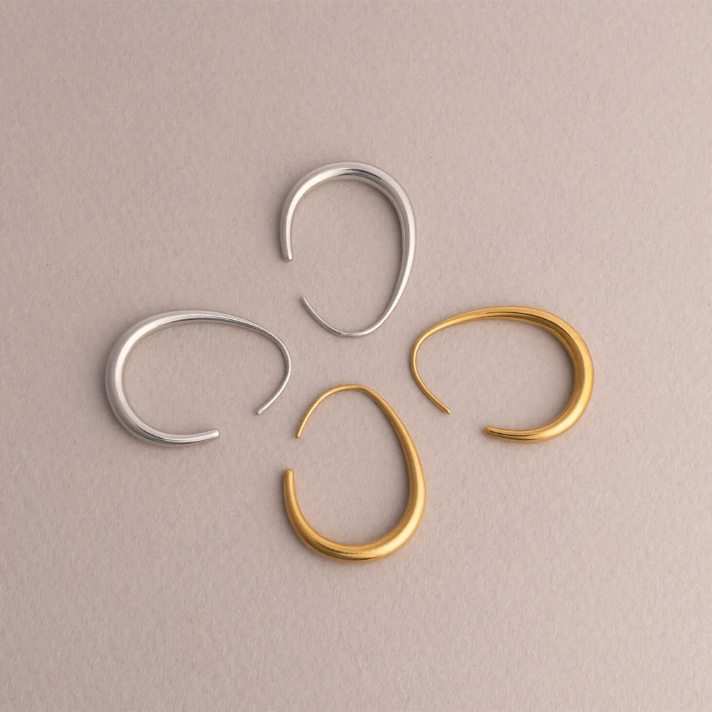 Three hoop earrings, two silver and one gold, on a beige background