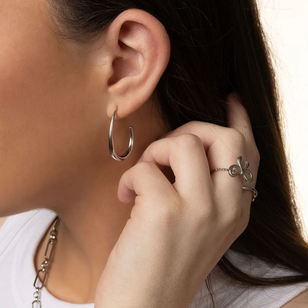 Close-up of a person wearing silver hoop earrings and a ring, with a neutral background.