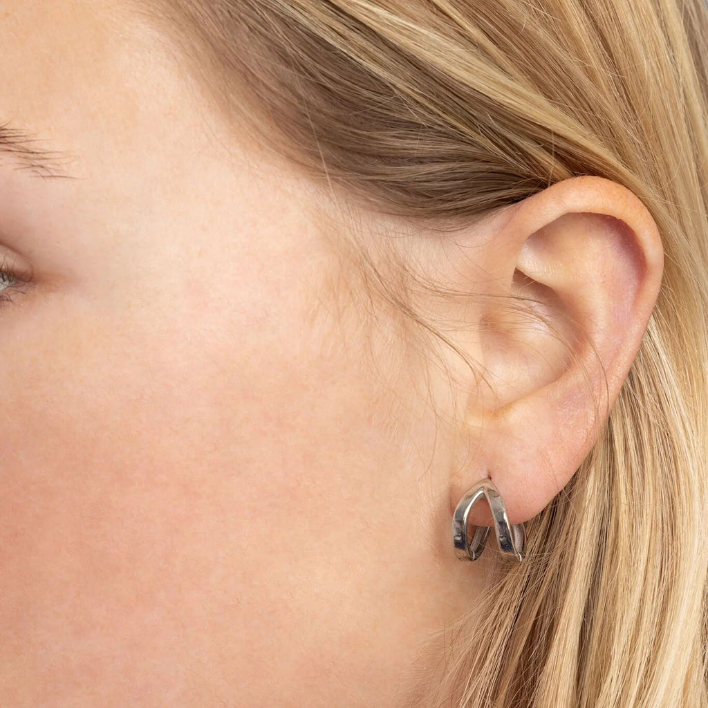 Close-up of an ear wearing a small silver hoop earring.