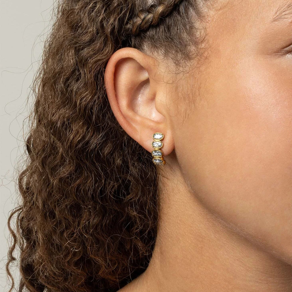 Close-up of an ear wearing a gold Oval Stone Huggie Earrings with three small stones.