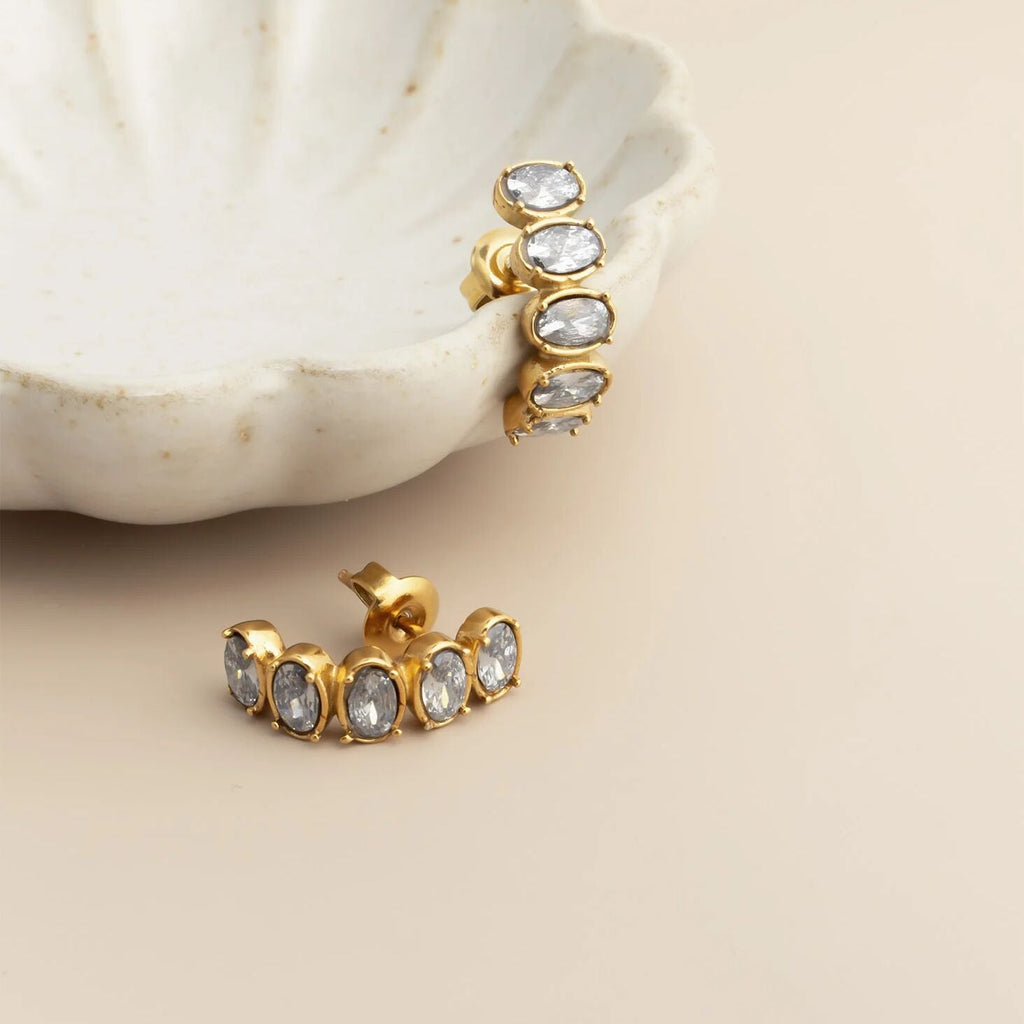 Gold Oval Stone Huggie Earrings with gemstones on a beige surface