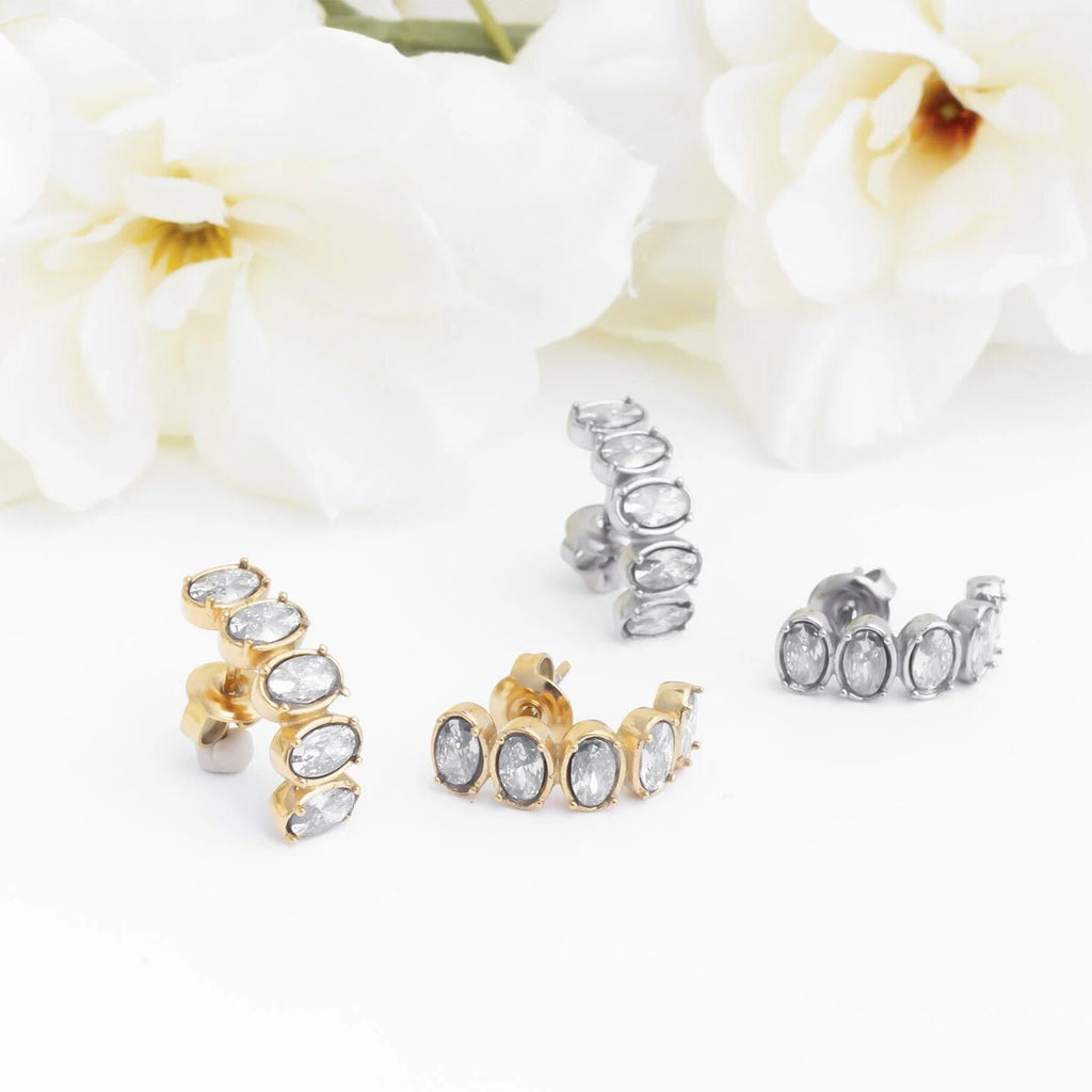 Gold and silver Oval Stone Huggie Earrings on a white background with flowers.