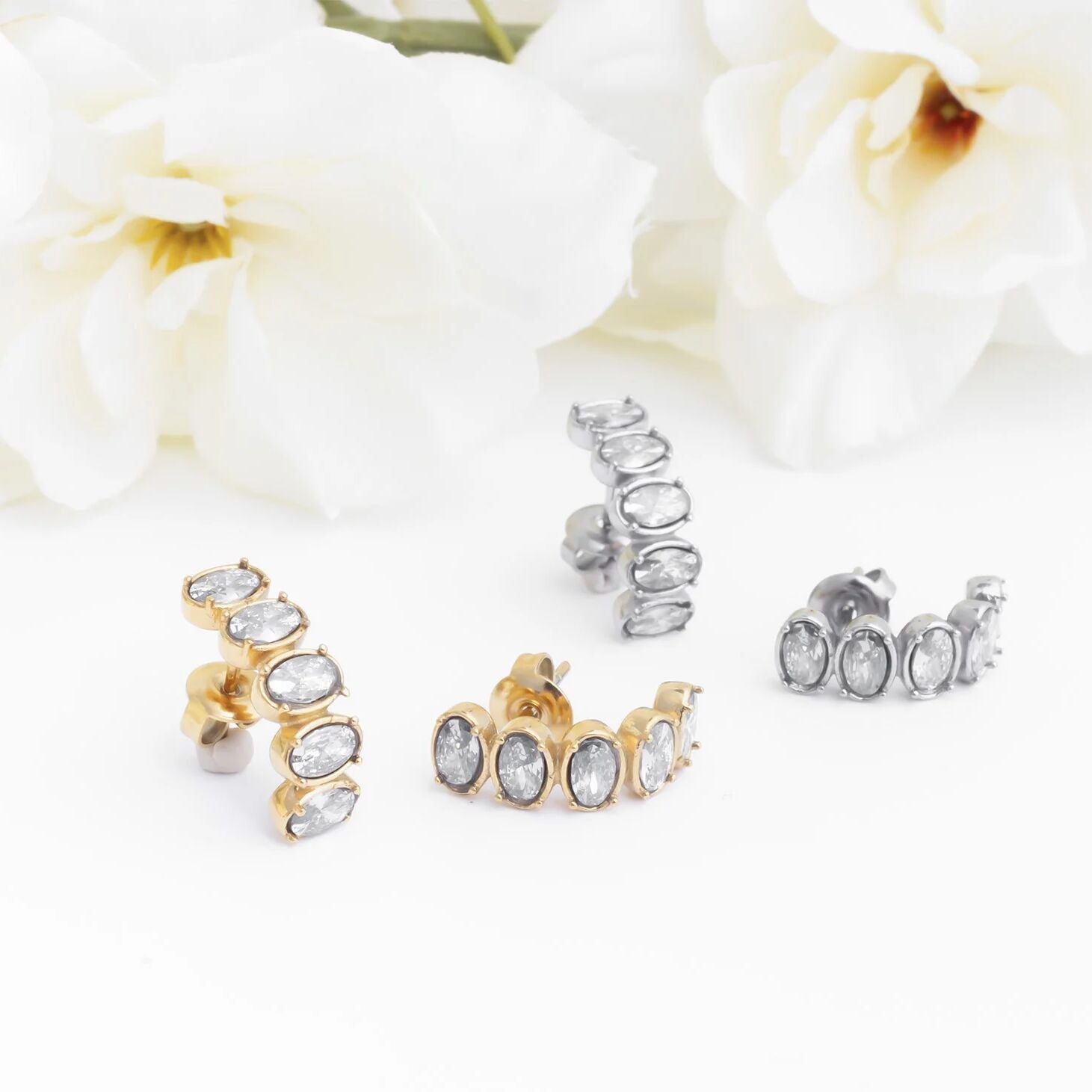 Gold and silver Oval Stone Huggie Earrings on a white background with flowers.