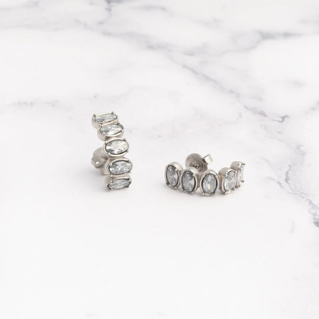 Pair of silver hoop Oval Stone Huggie Earrings with clear gemstones on a marble surface