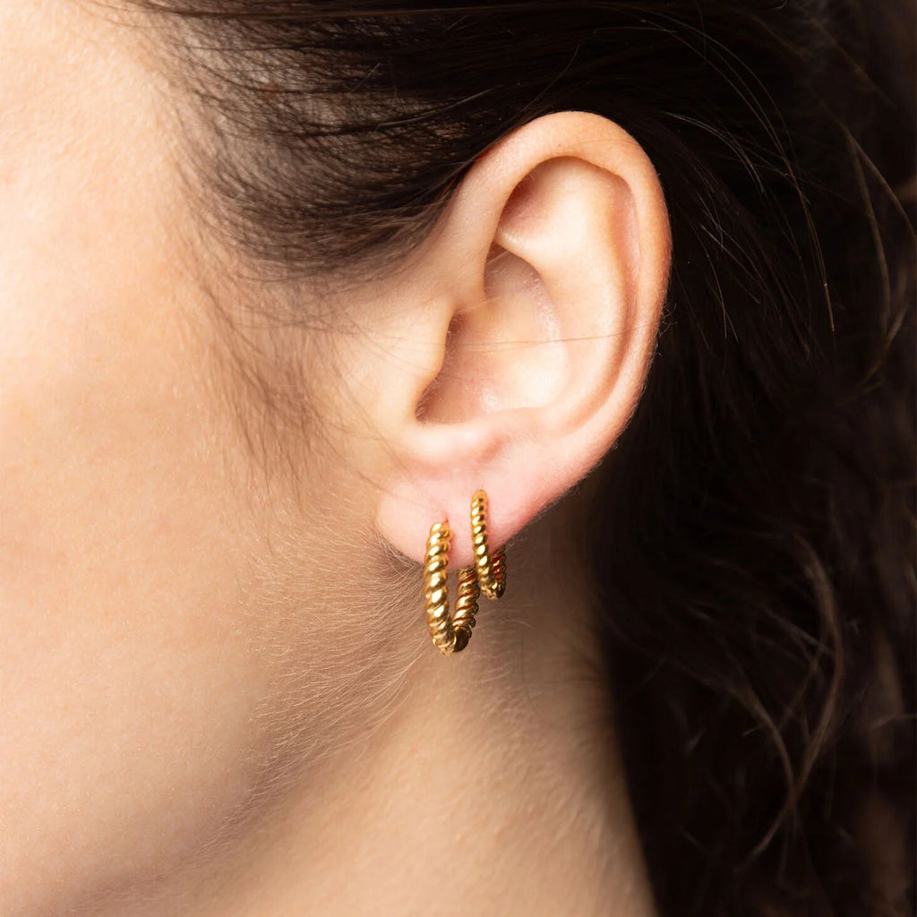 Close-up of an ear wearing gold hoop earrings with a blurred background