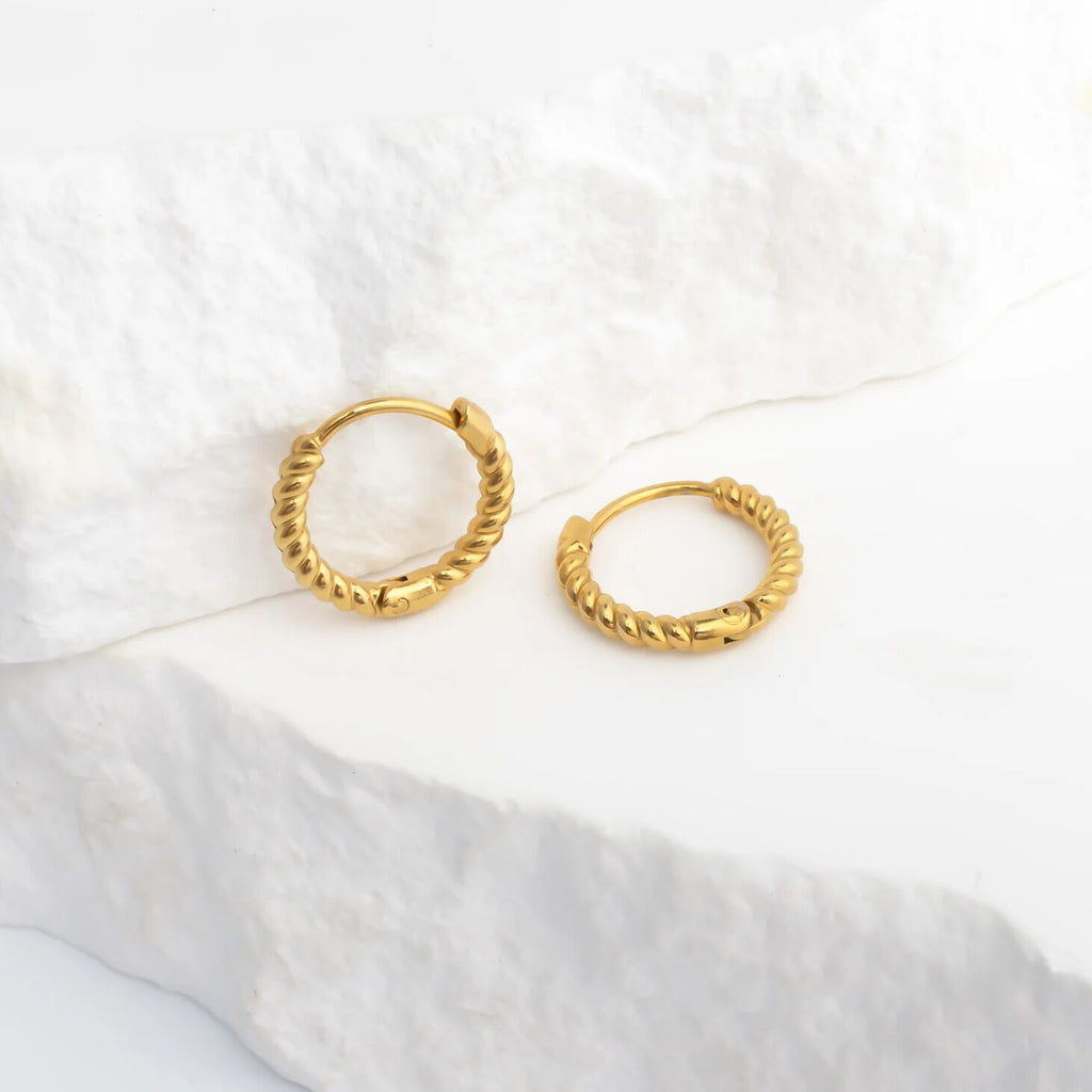 Gold hoop earrings on a white fabric background