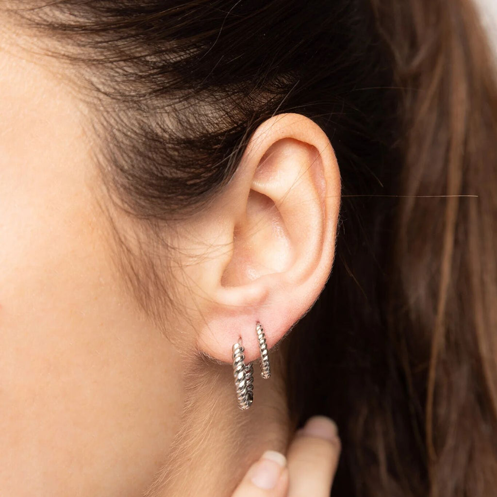 Close-up of an ear wearing two silver hoop earrings with a blurred background