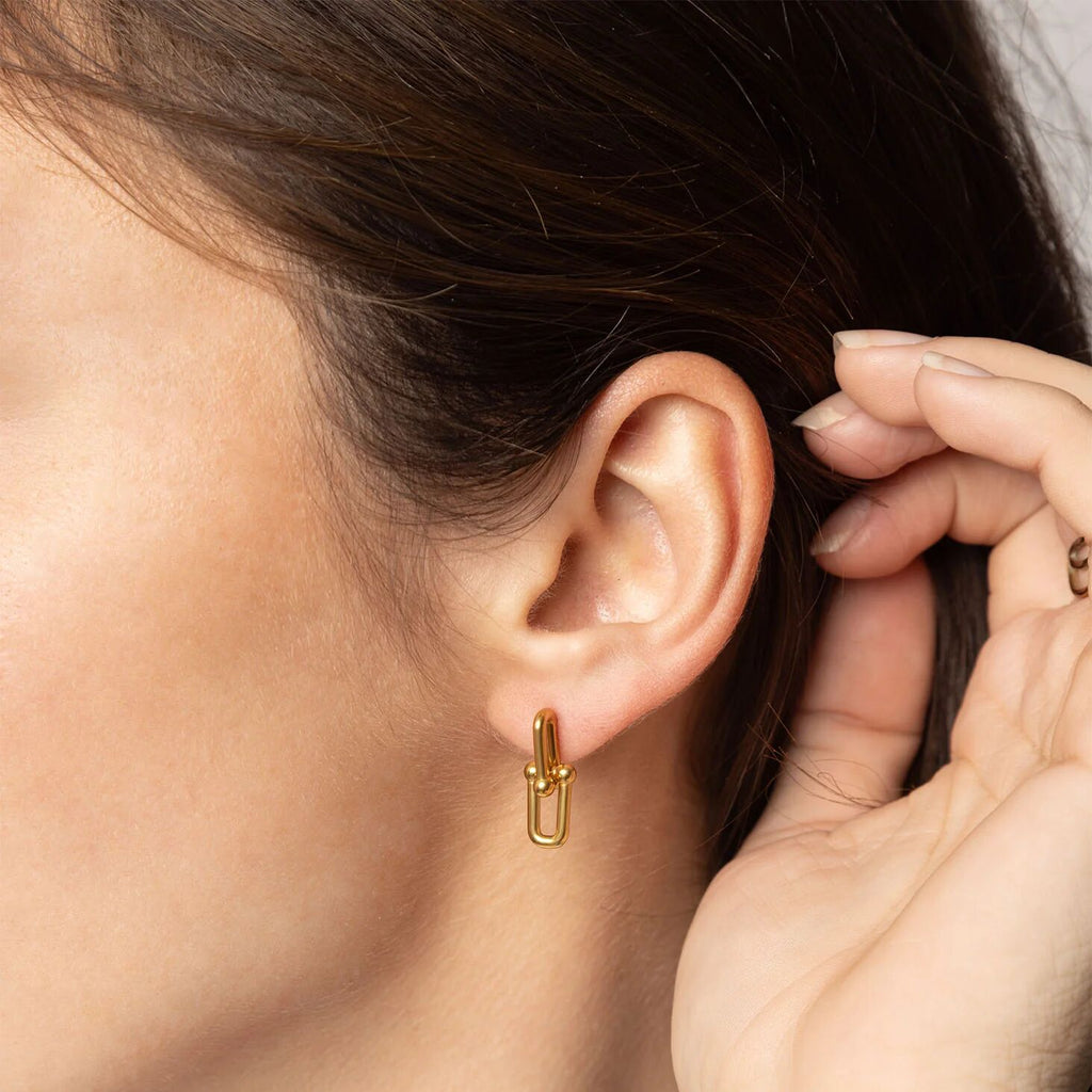 Gold earring worn by a person with a close-up of the ear and hand.