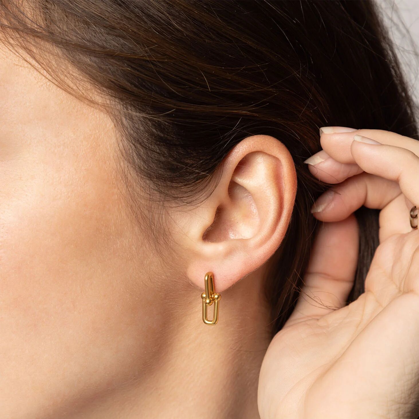 Gold earring worn by a person with a close-up of the ear and hand.