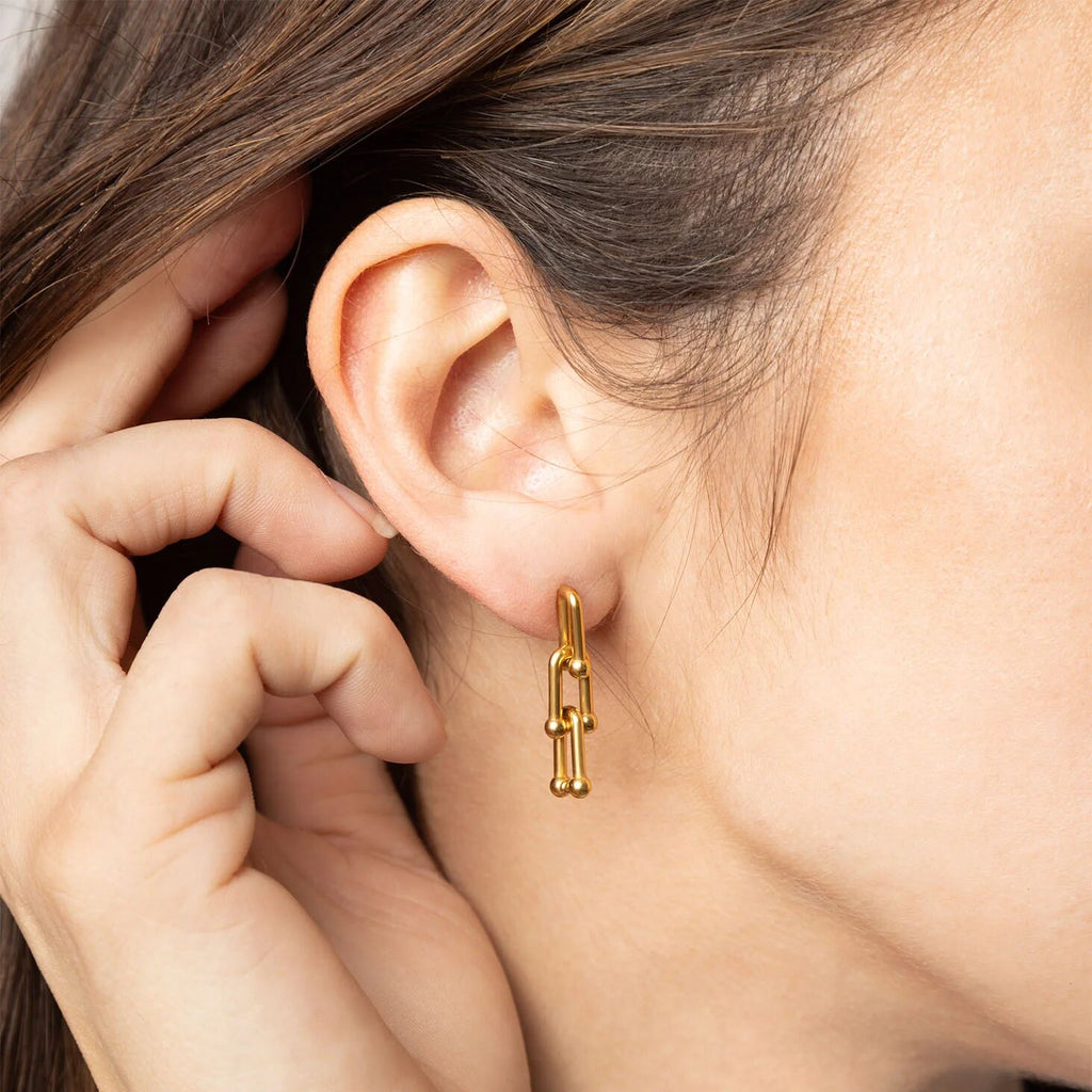 Close-up of a person wearing a gold hoop earring with their hand near their ear.