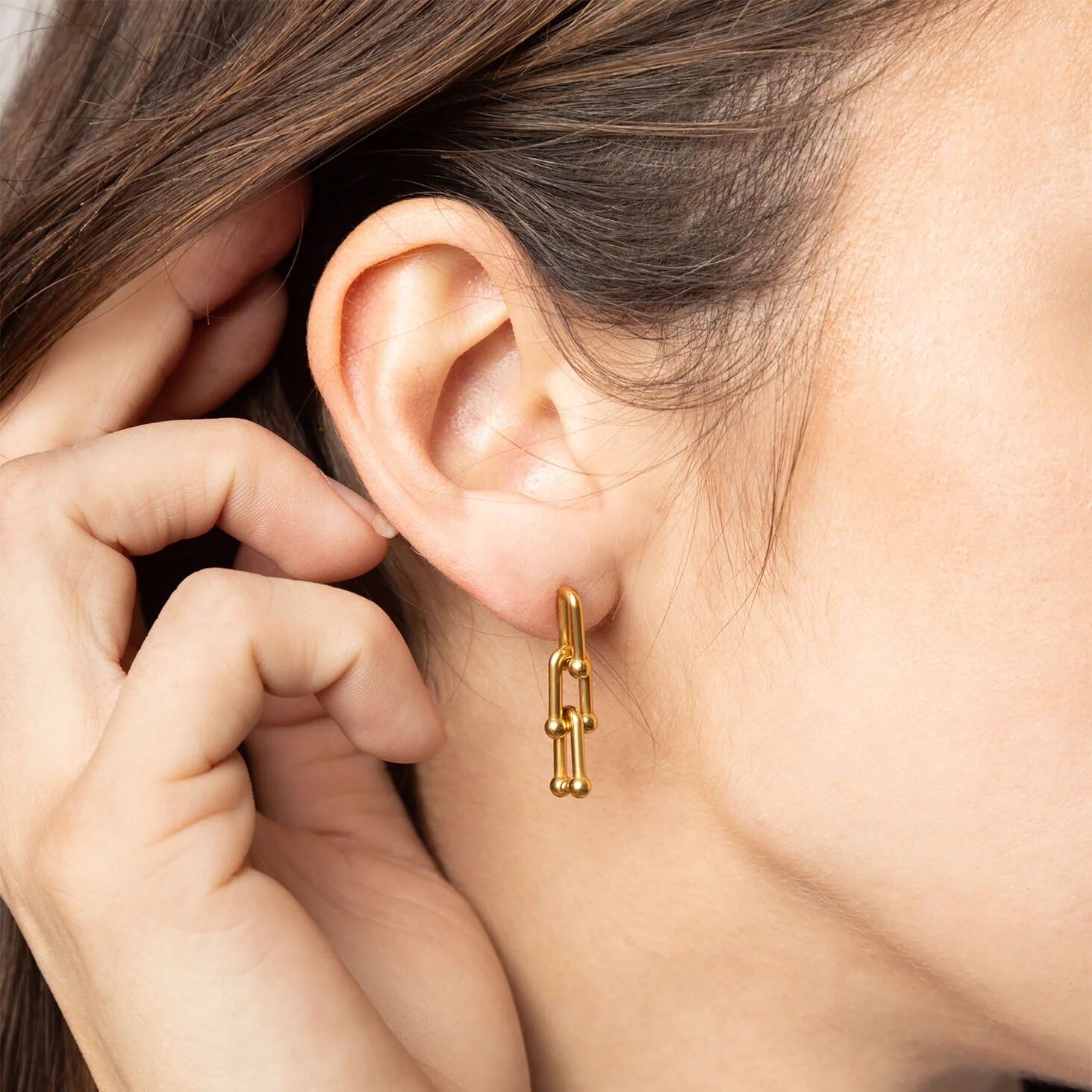 Close-up of a person wearing a gold hoop earring with their hand near their ear.
