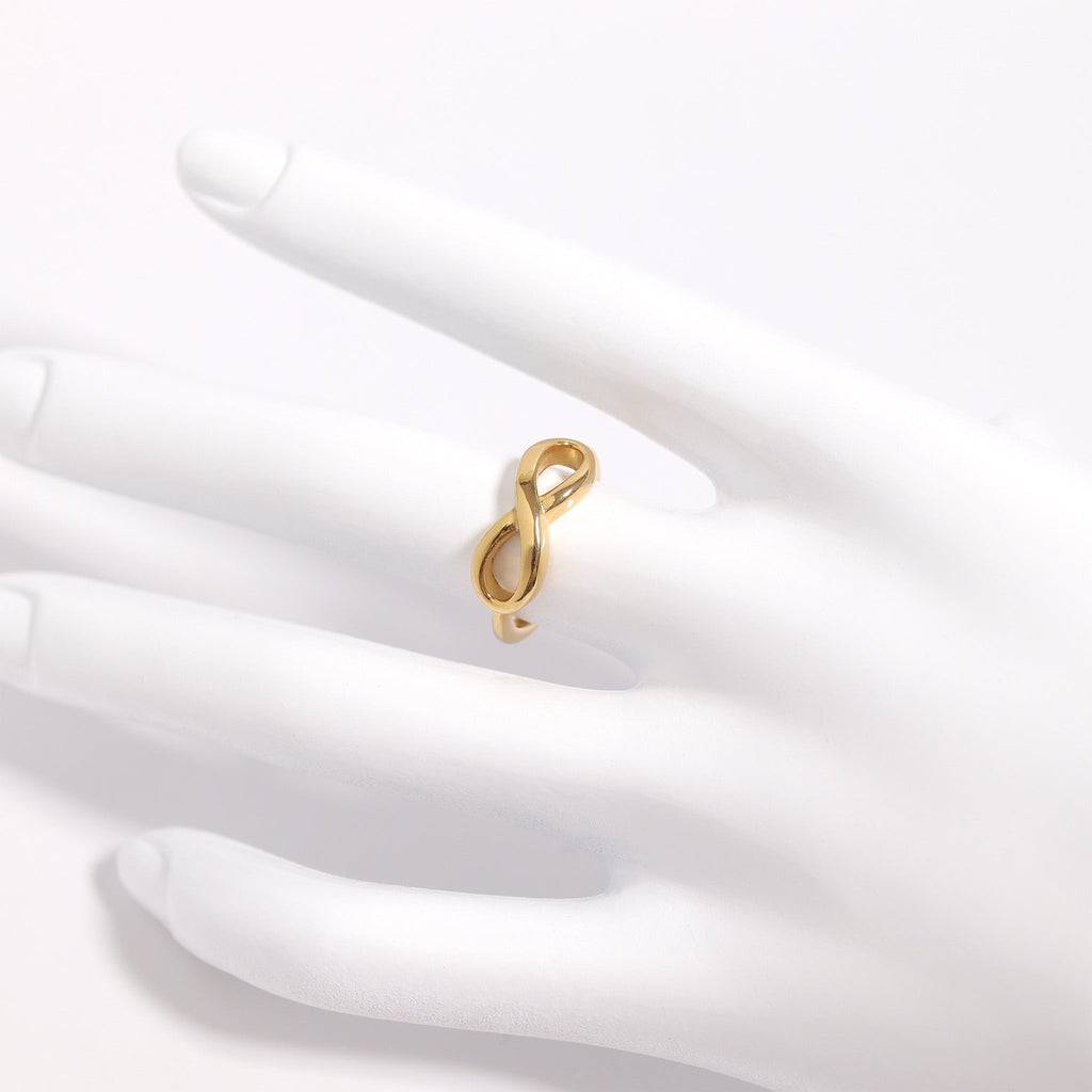 A gold ring with an intricate design is displayed on a white mannequin hand.