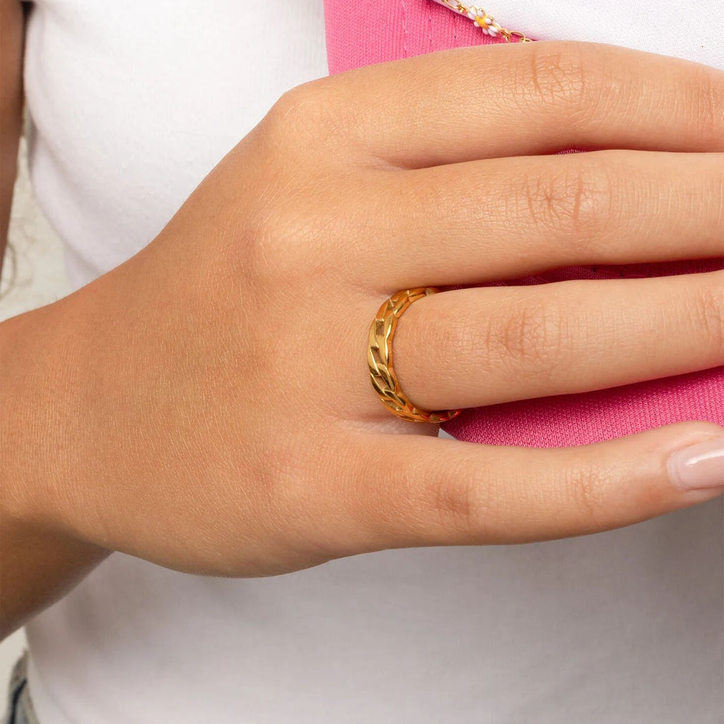Hand wearing a gold Curb Chain Stacking Ring with a pink object in the background