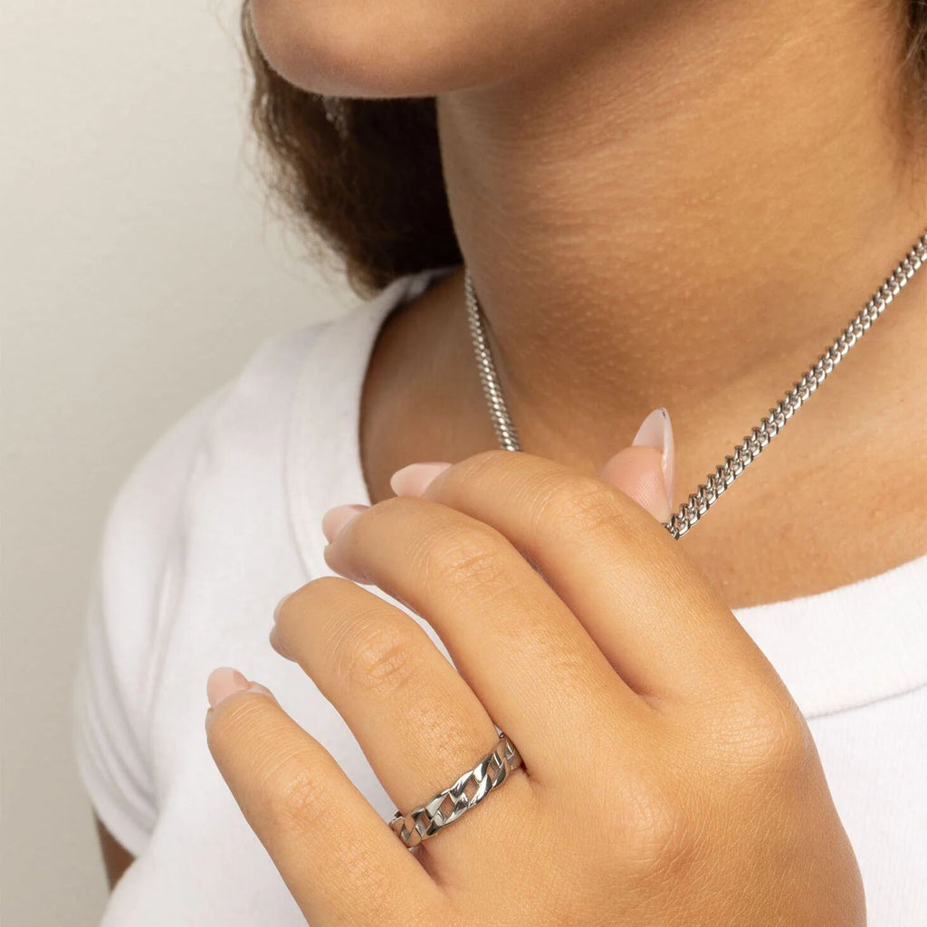 Close-up of a person wearing a silver necklace and Curb Chain Stacking Ring on a plain background
