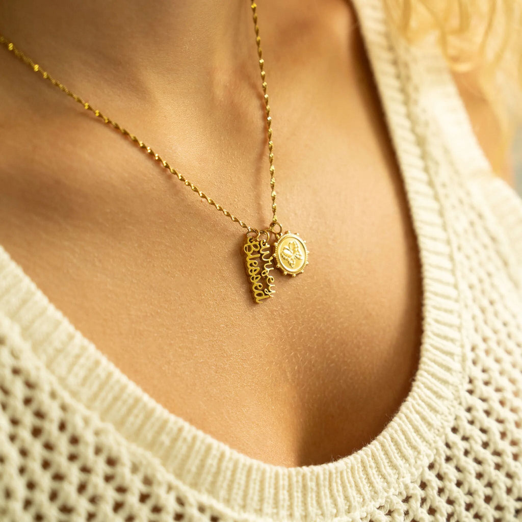 Gold necklace with heart-shaped pendants worn by a person in a beige sweater.