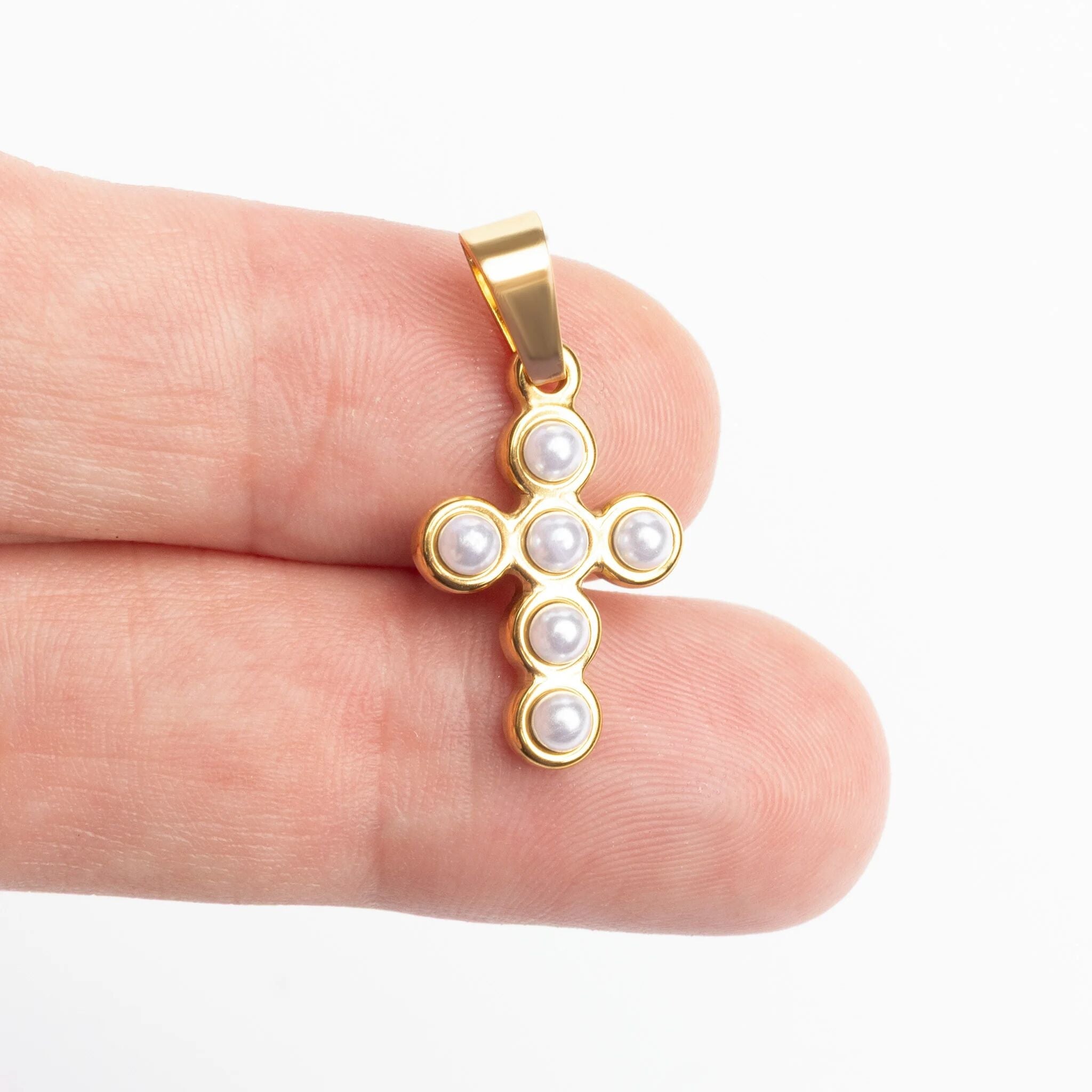 Gold cross pendant with pearls held between fingers on a white background for scale