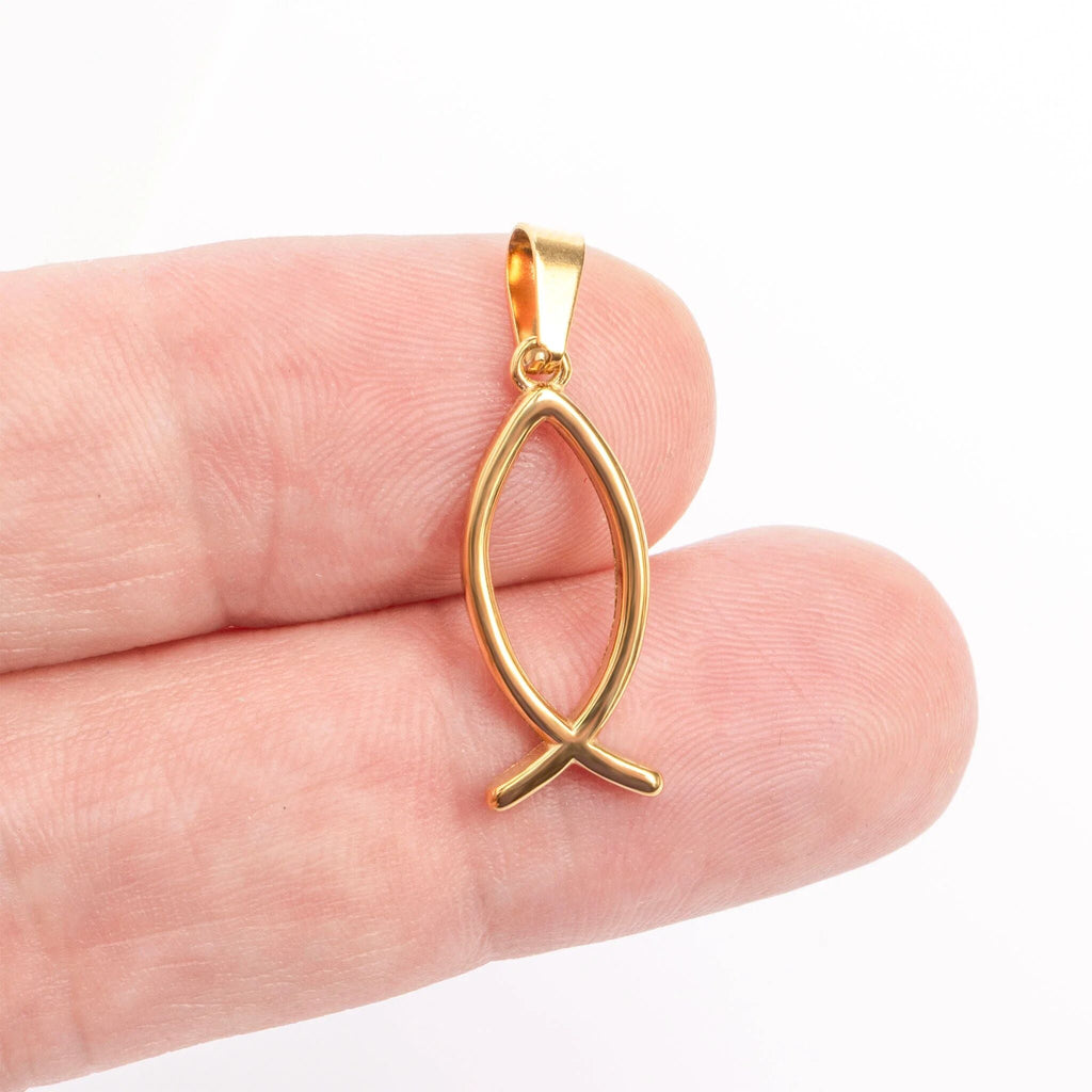 Gold fish-shaped pendant held between fingers on a white background