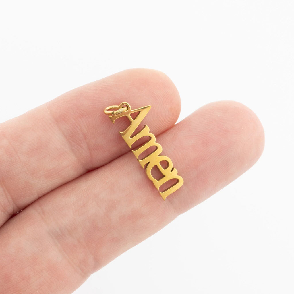 Gold 'Amen' pendant held between fingers on a white background
