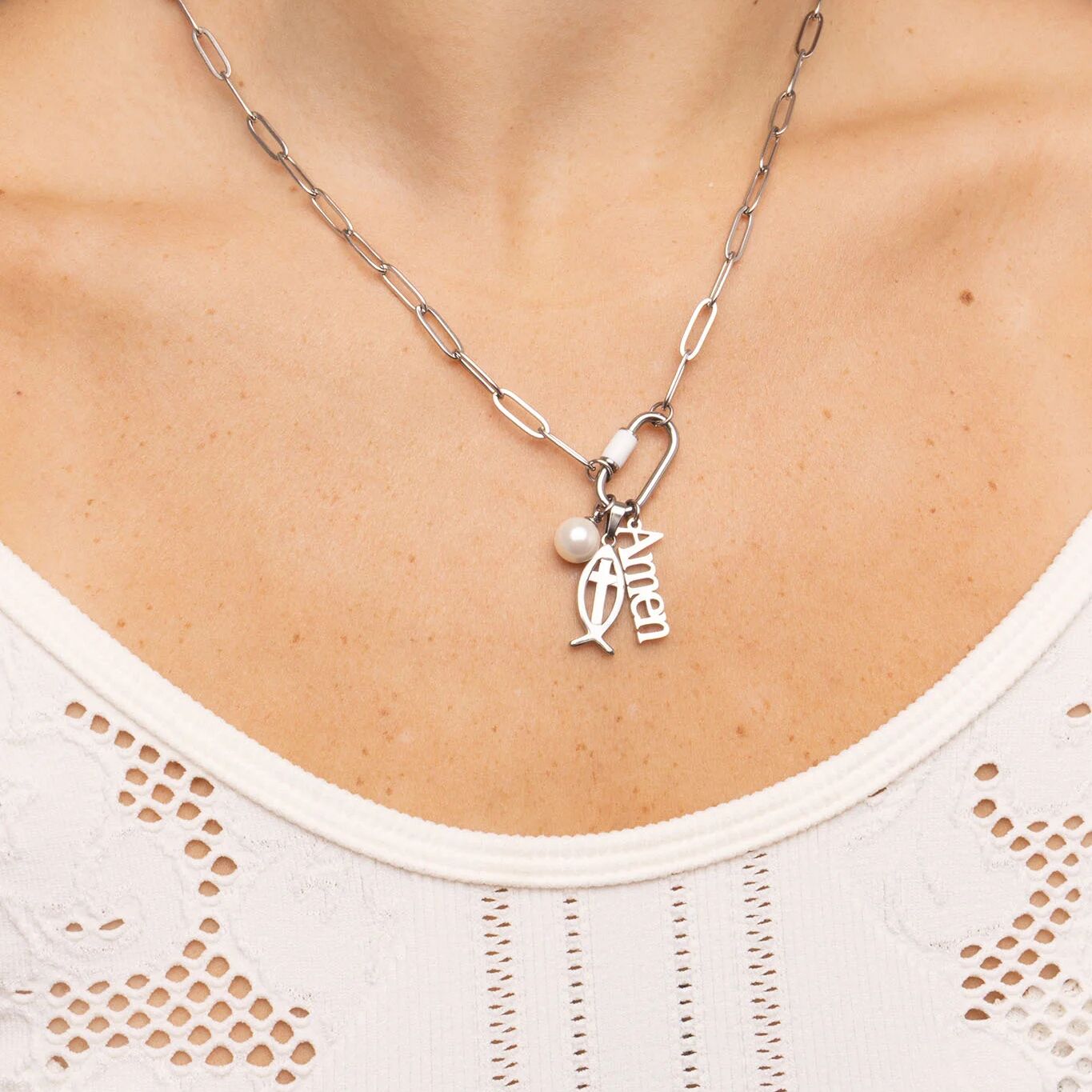 Silver necklace with a pendant and pearl on a person wearing a white top.