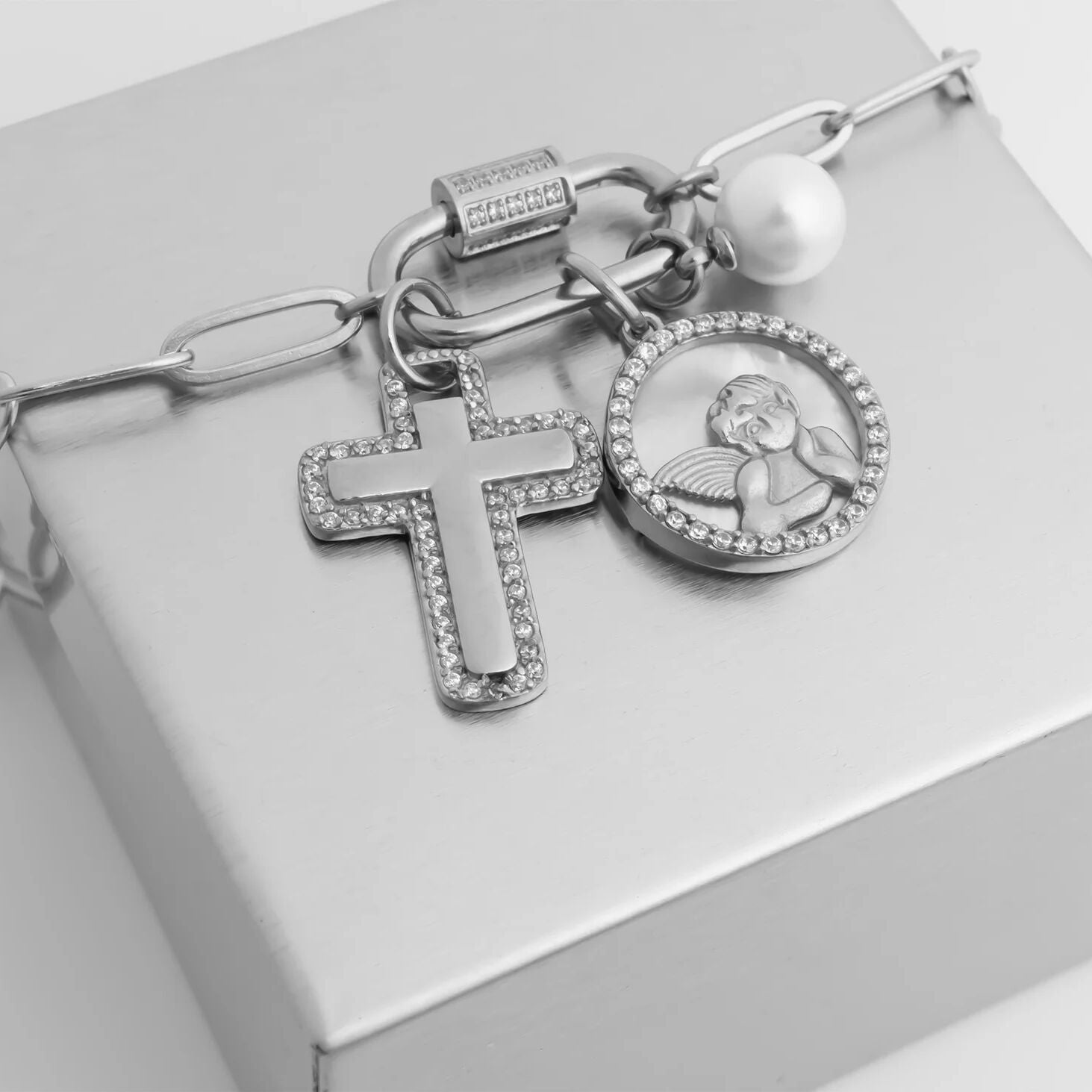 Silver charm bracelet with cross and circular charm on a light gray background
