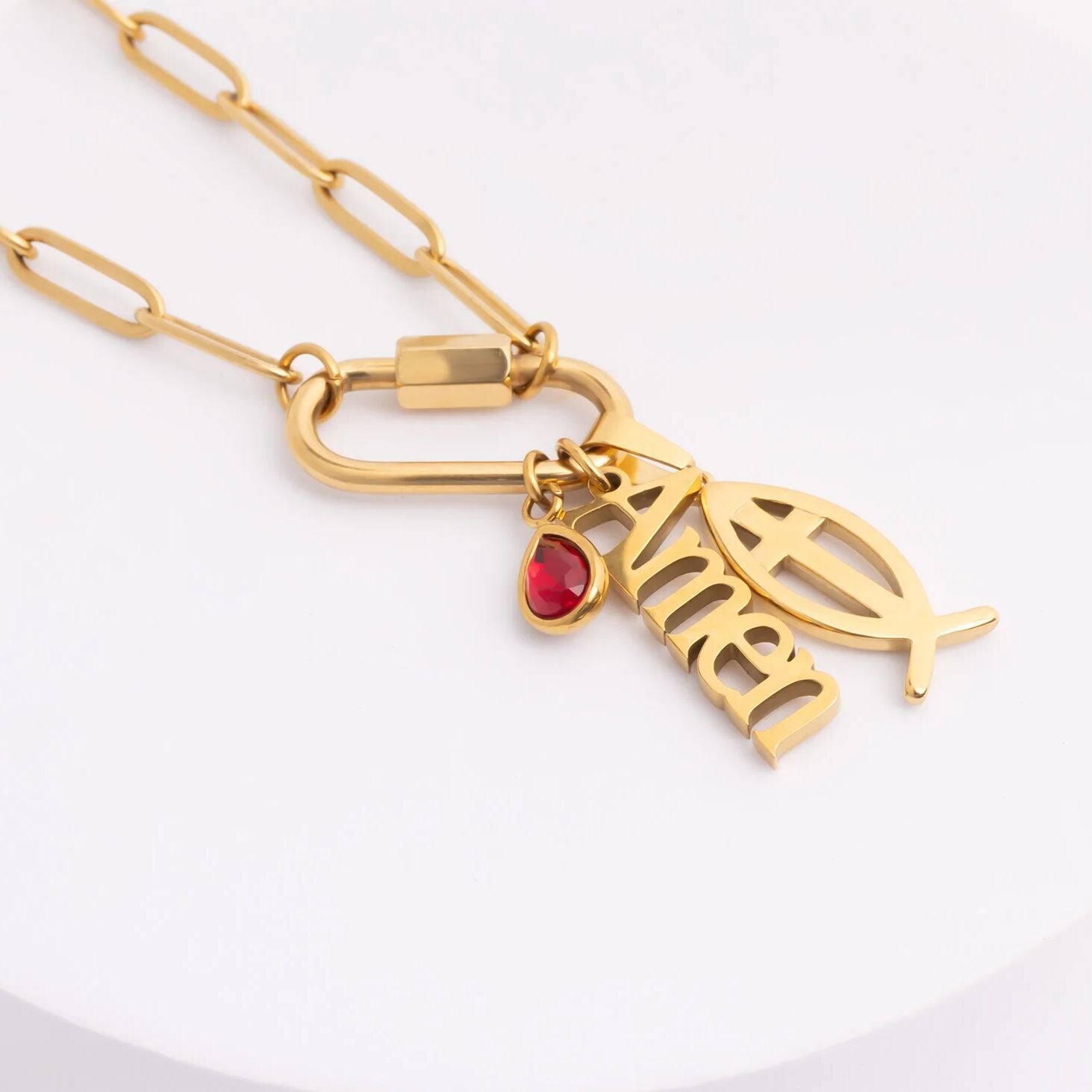 Gold necklace with a fish charm and red gemstone on a white background