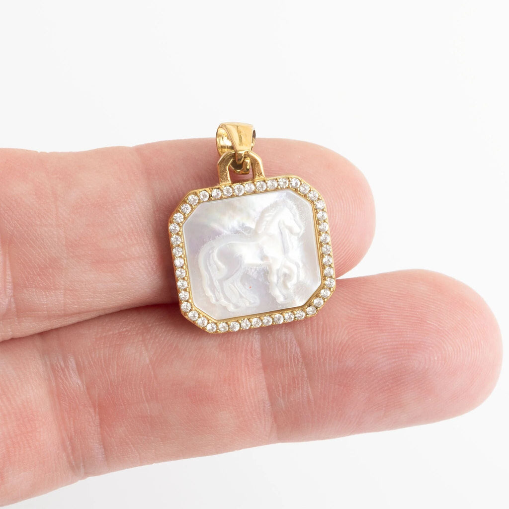 Gold pendant with a white stone held between fingers on a white background