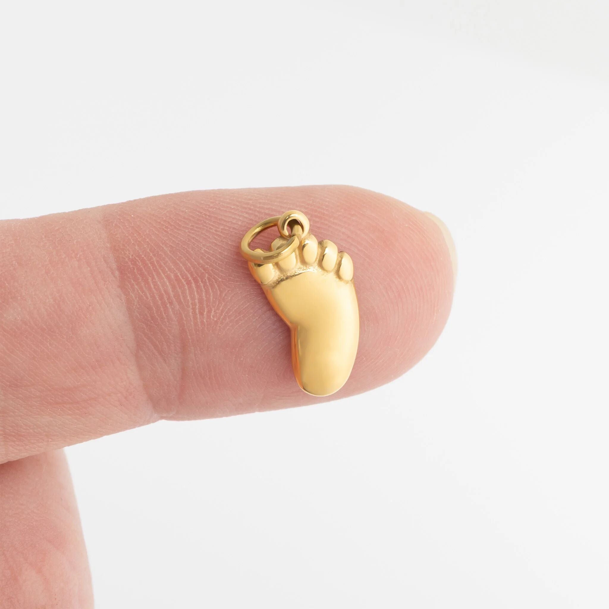 Gold baby foot-shaped charm on a finger against a white background for scale