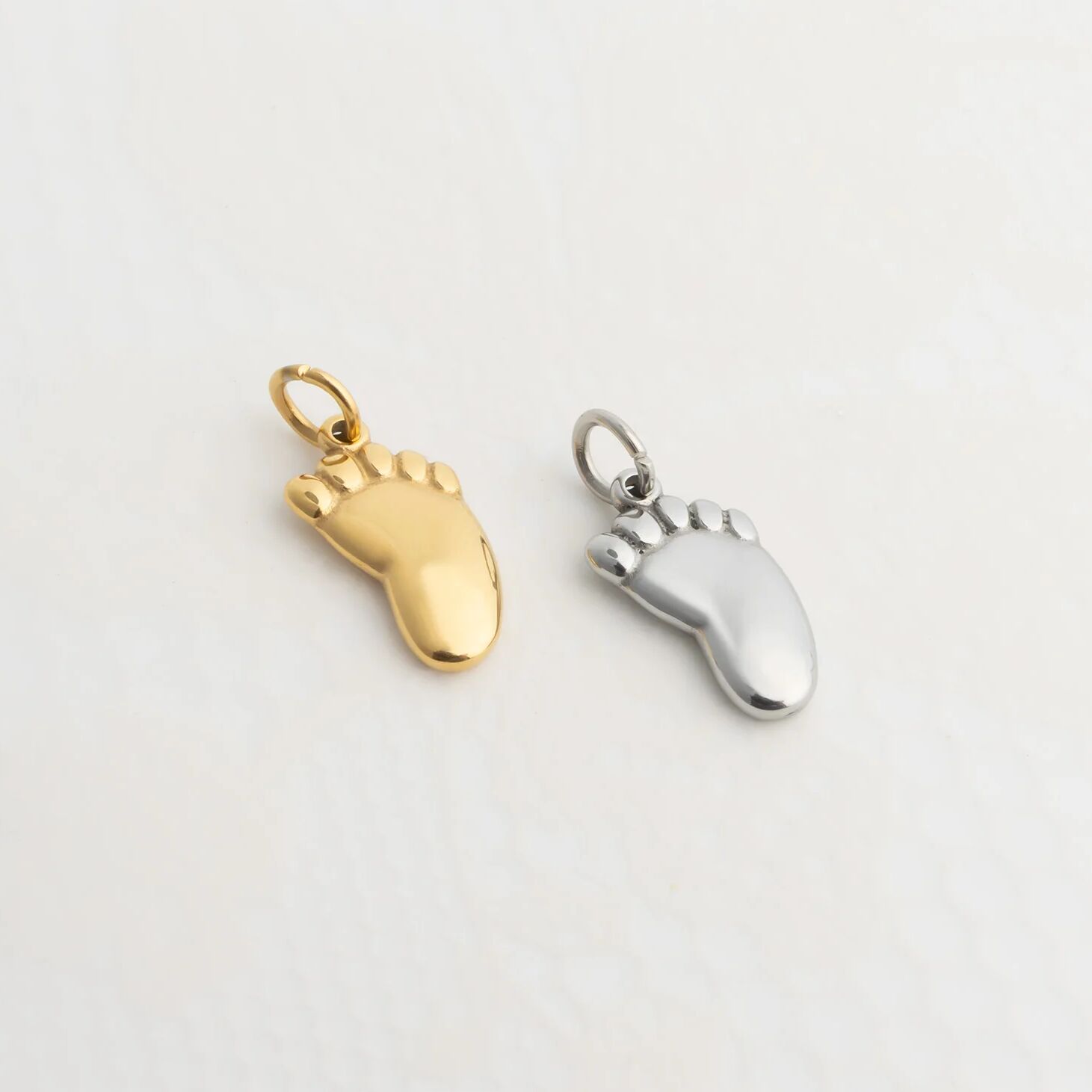 Gold and silver Baby Foot Charm on a light gray background