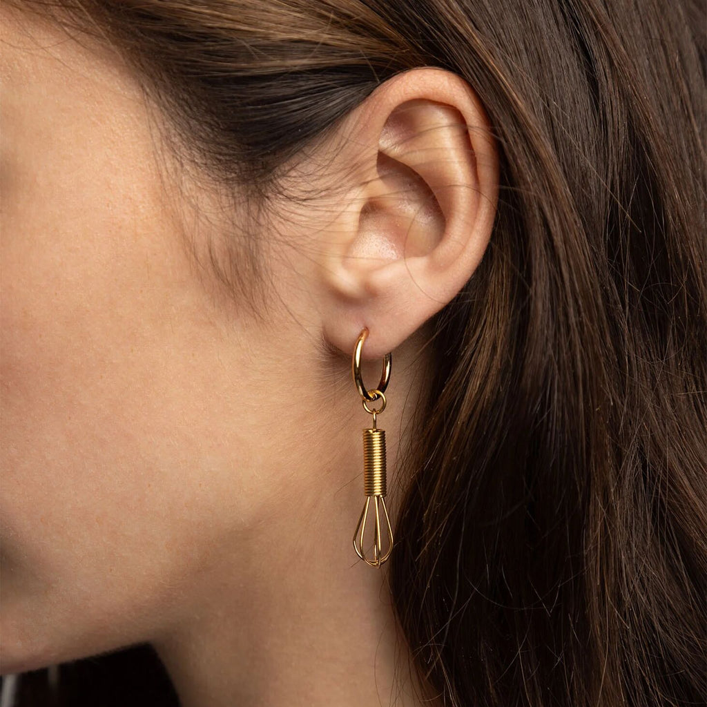 Gold hoop earring with a dangling component worn by a person.