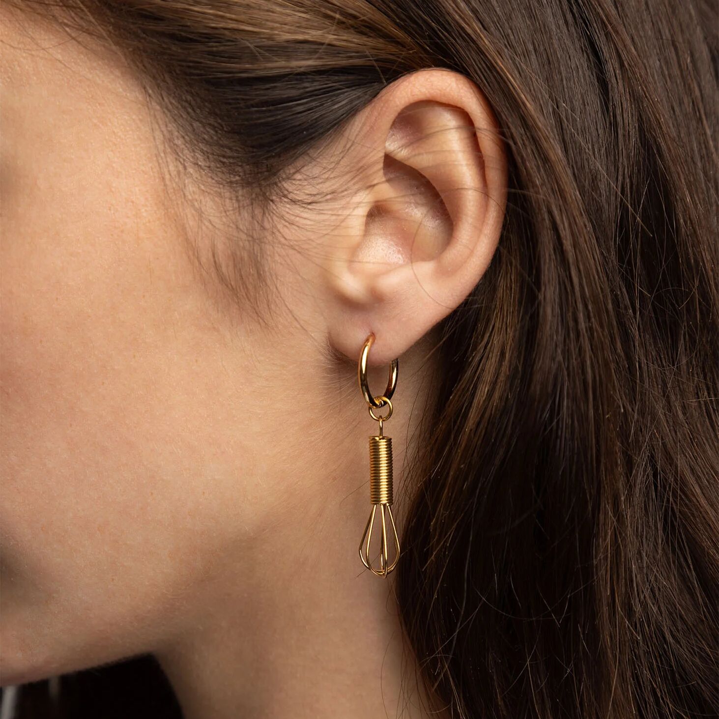 Gold hoop earring with a dangling component worn by a person.