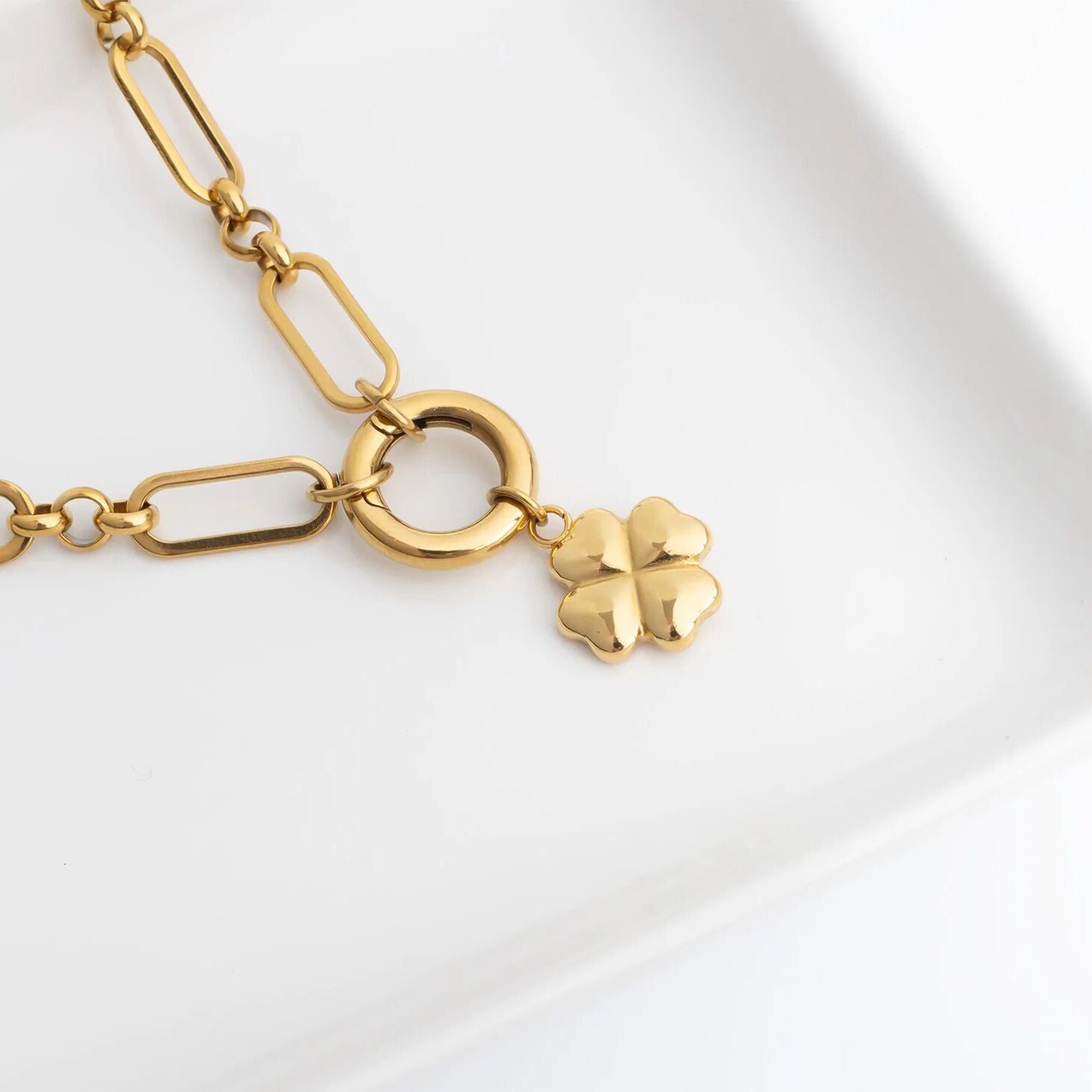 Gold necklace with a clover charm on a white background