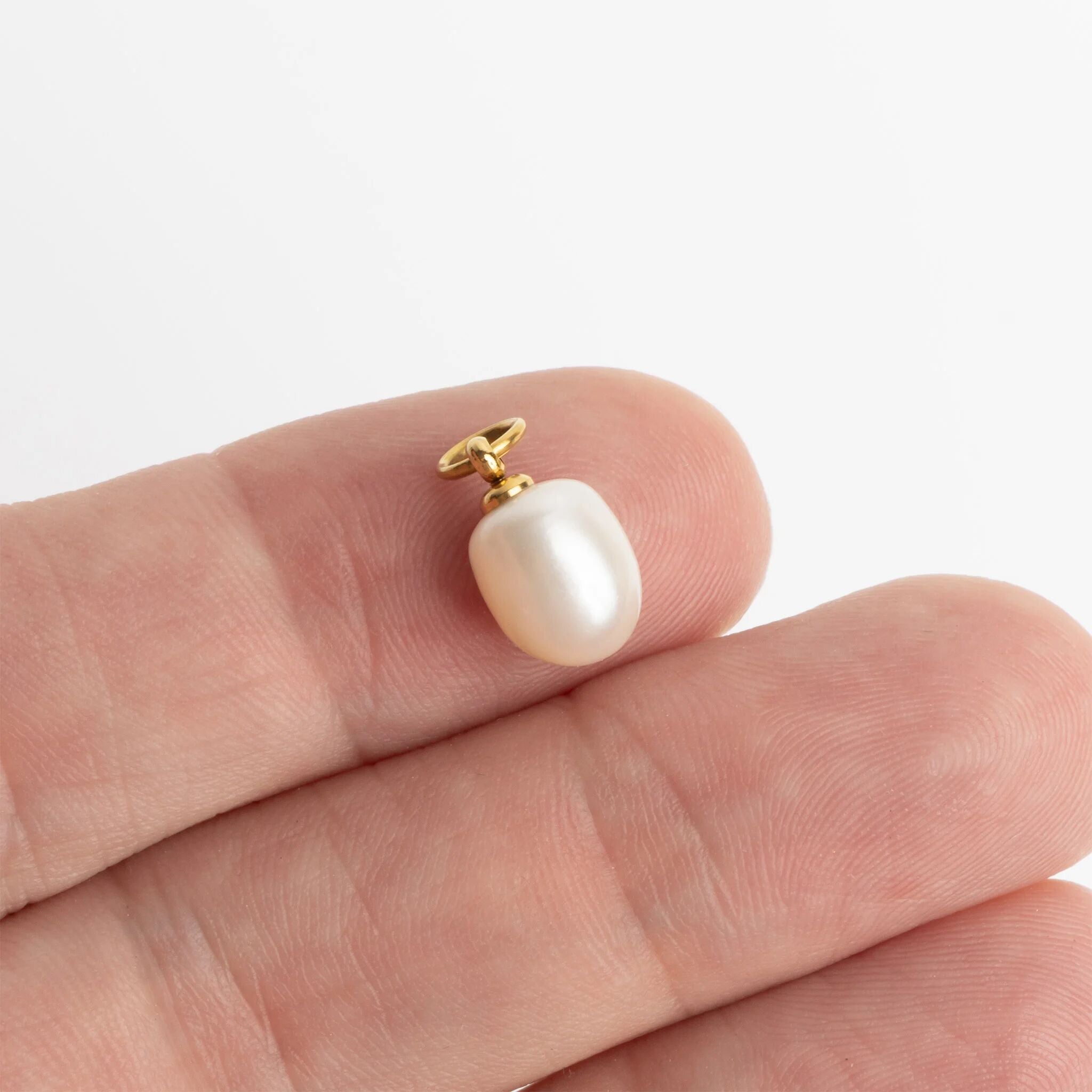 Pearl pendant on a gold chain held between fingers against a white background
