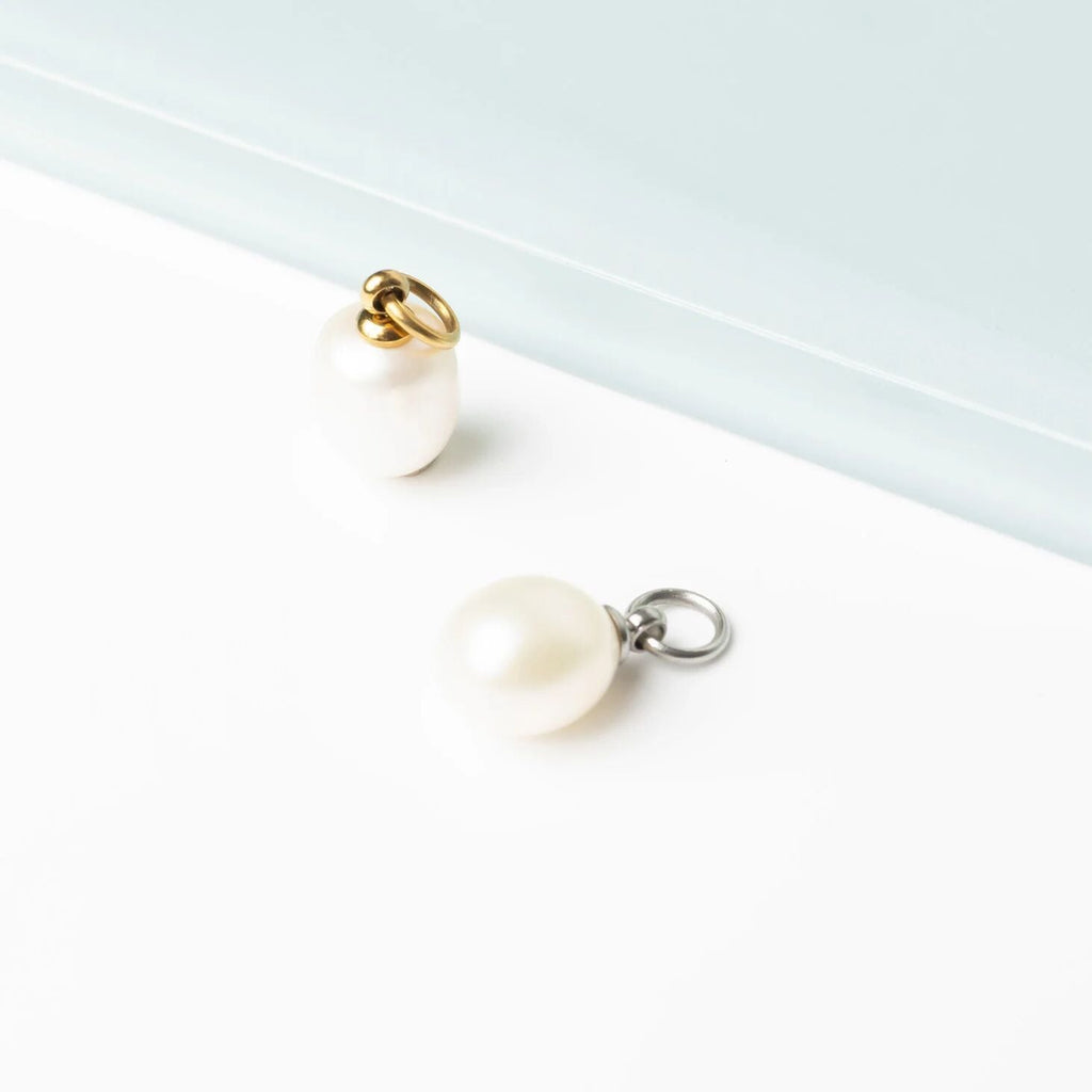 Pair of earrings with white shell-like pendants on gold and silver hooks against a light background