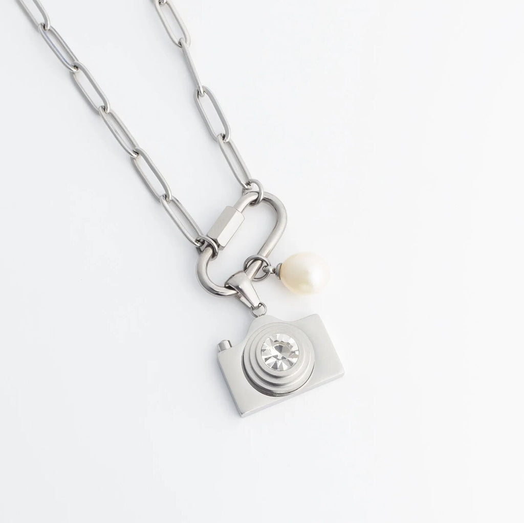 Silver necklace with a camera charm and pearl on a white background