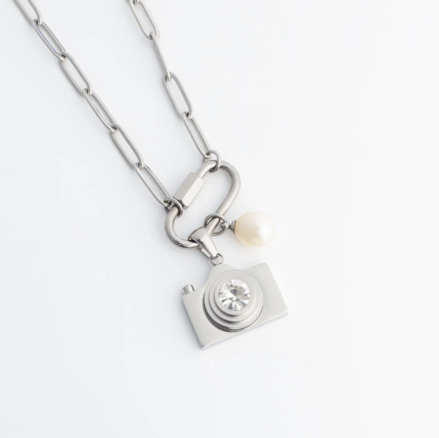 Silver necklace with a camera charm and pearl on a white background