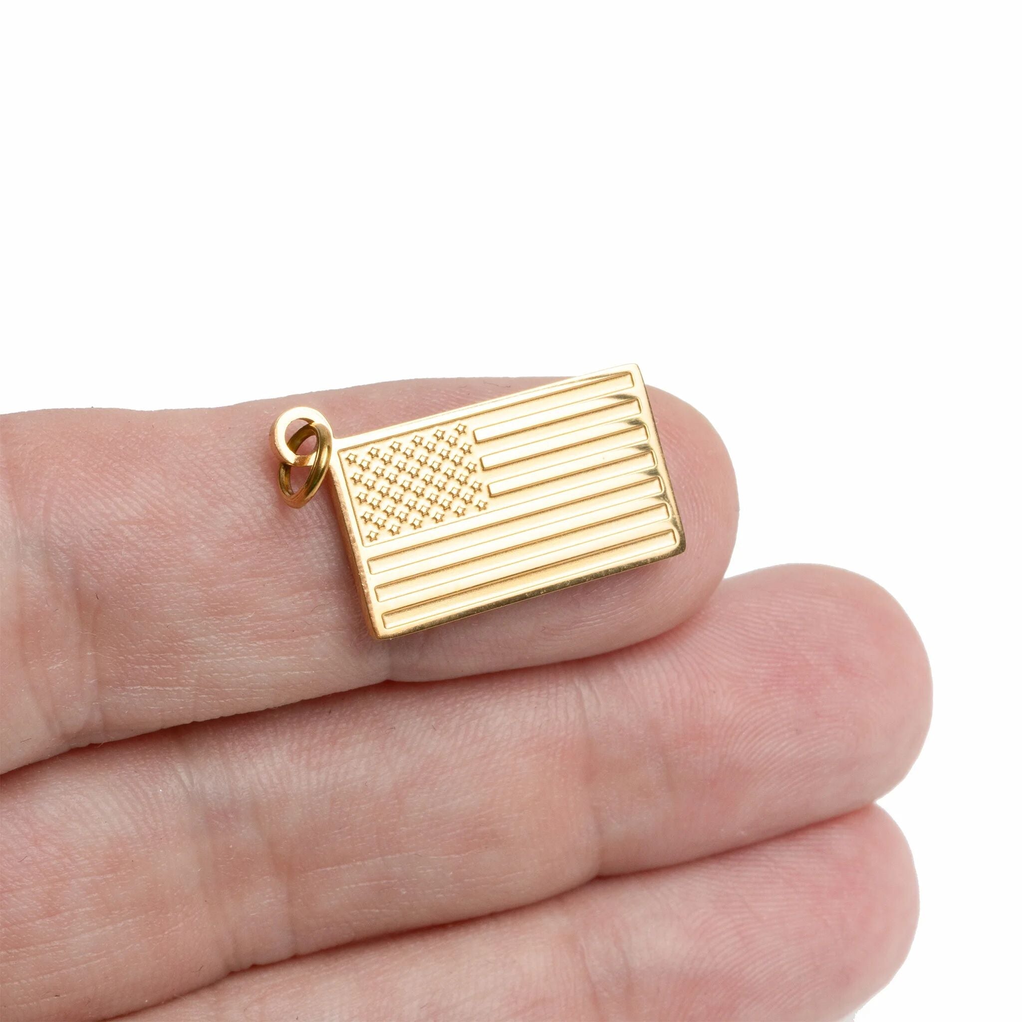 Gold American flag pendant held between fingers on a white background
