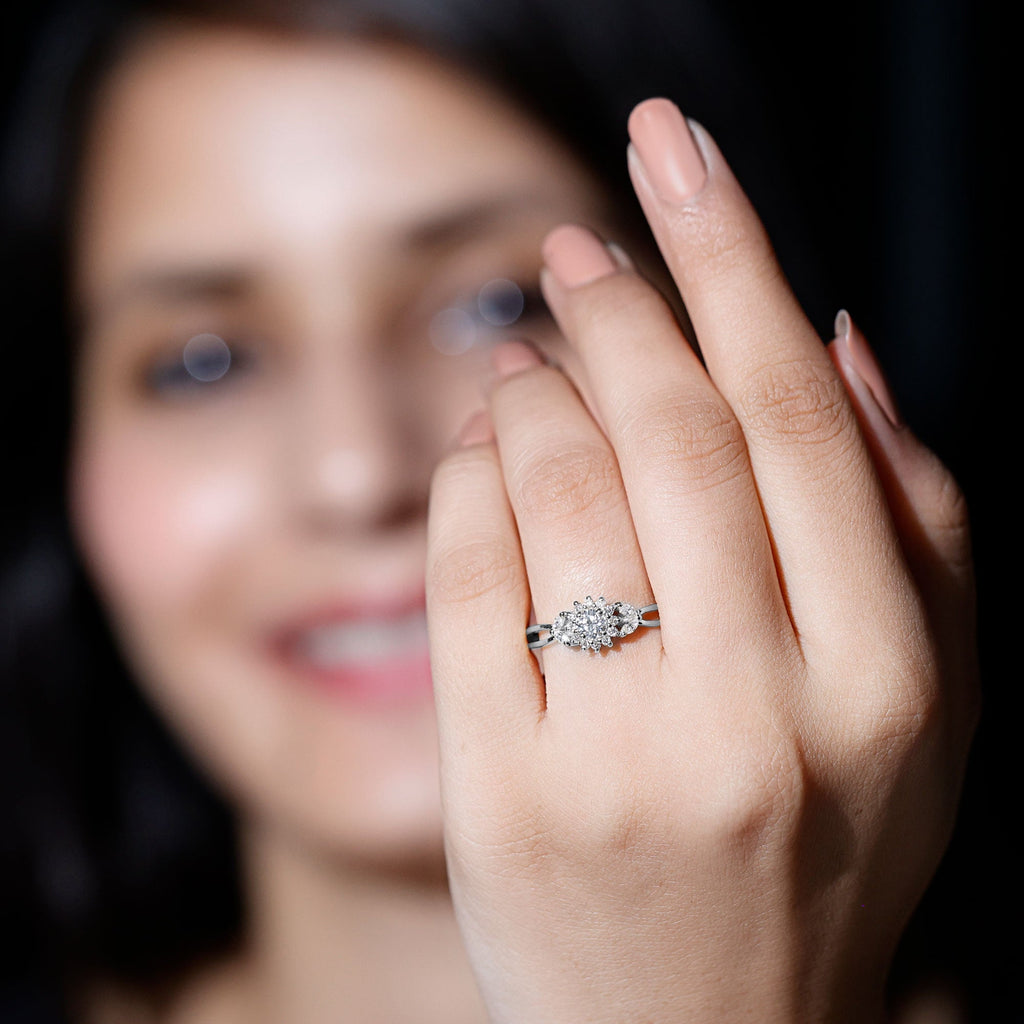 A close-up of a person's hand wearing a diamond engagement ring, with a blurred background.