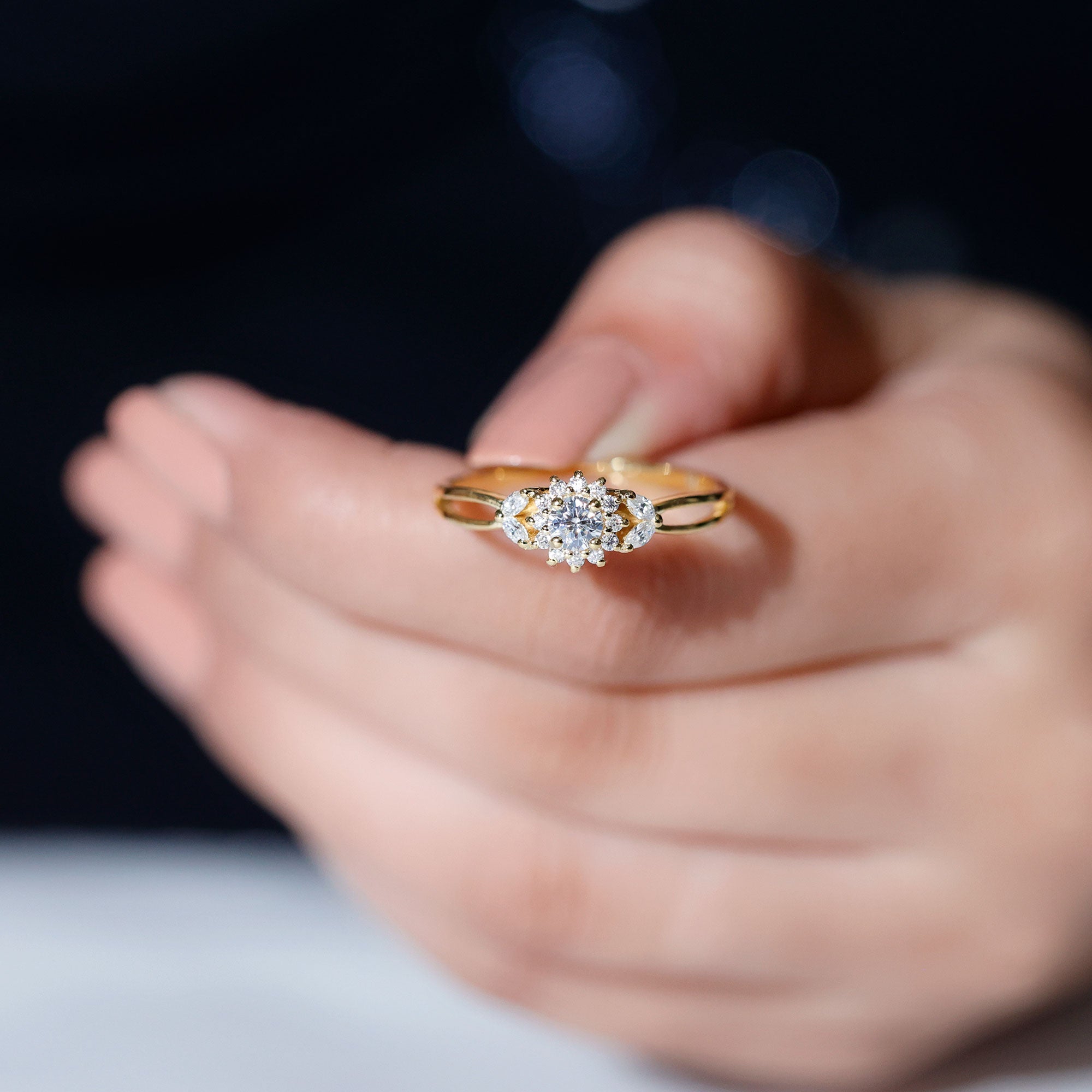 A close-up image of a person's hand holding a gold ring with a diamond center stone.