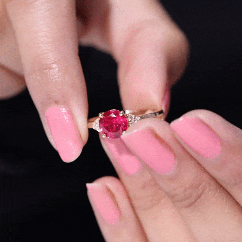 Lab grown ruby solitaire engagement ring with diamond trio held between fingers