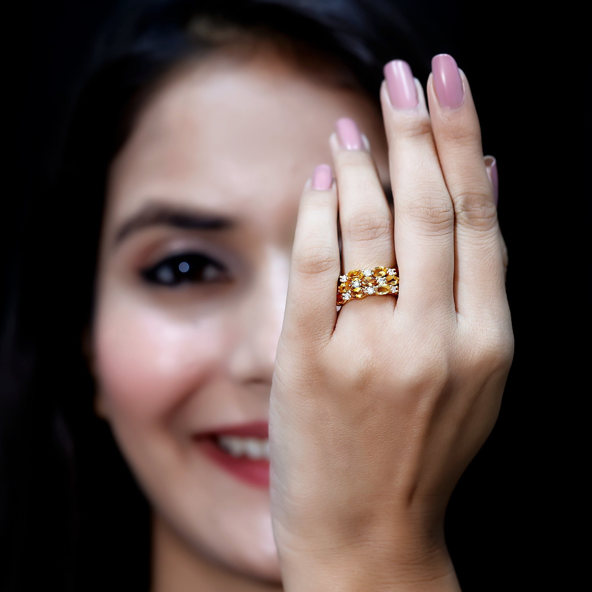 A woman with a smile on her face is holding up a gold ring with a floral design.