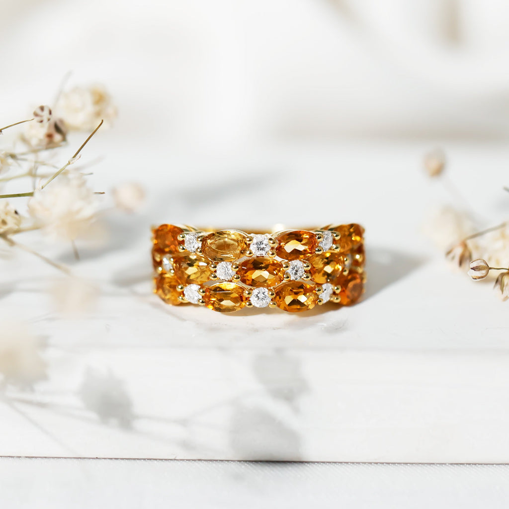 A gold ring with a large cluster of yellow and orange gemstones, including diamonds, is displayed on a white surface.