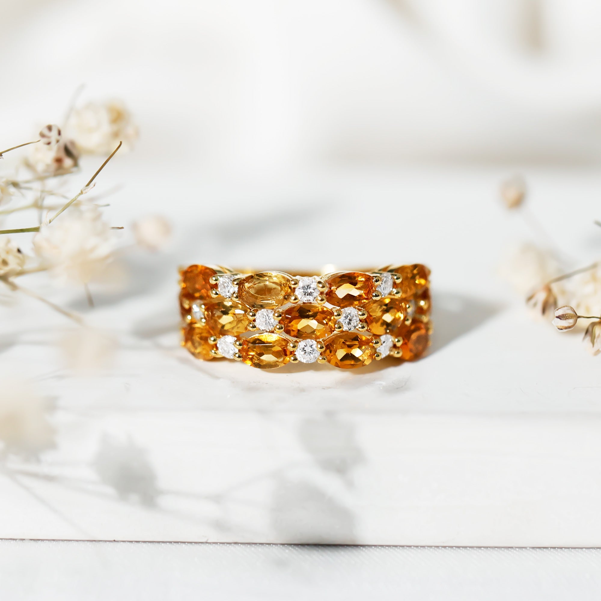 A gold ring with a large cluster of yellow and orange gemstones, including diamonds, is displayed on a white surface.