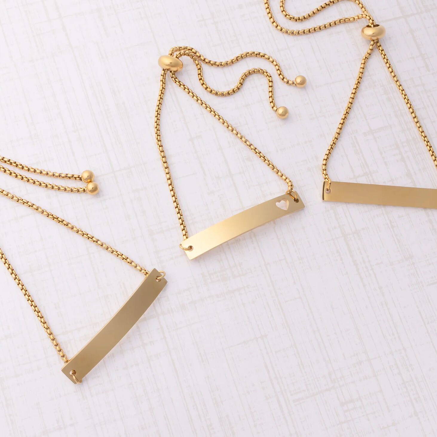 Gold necklaces with bar and heart pendants on a white surface