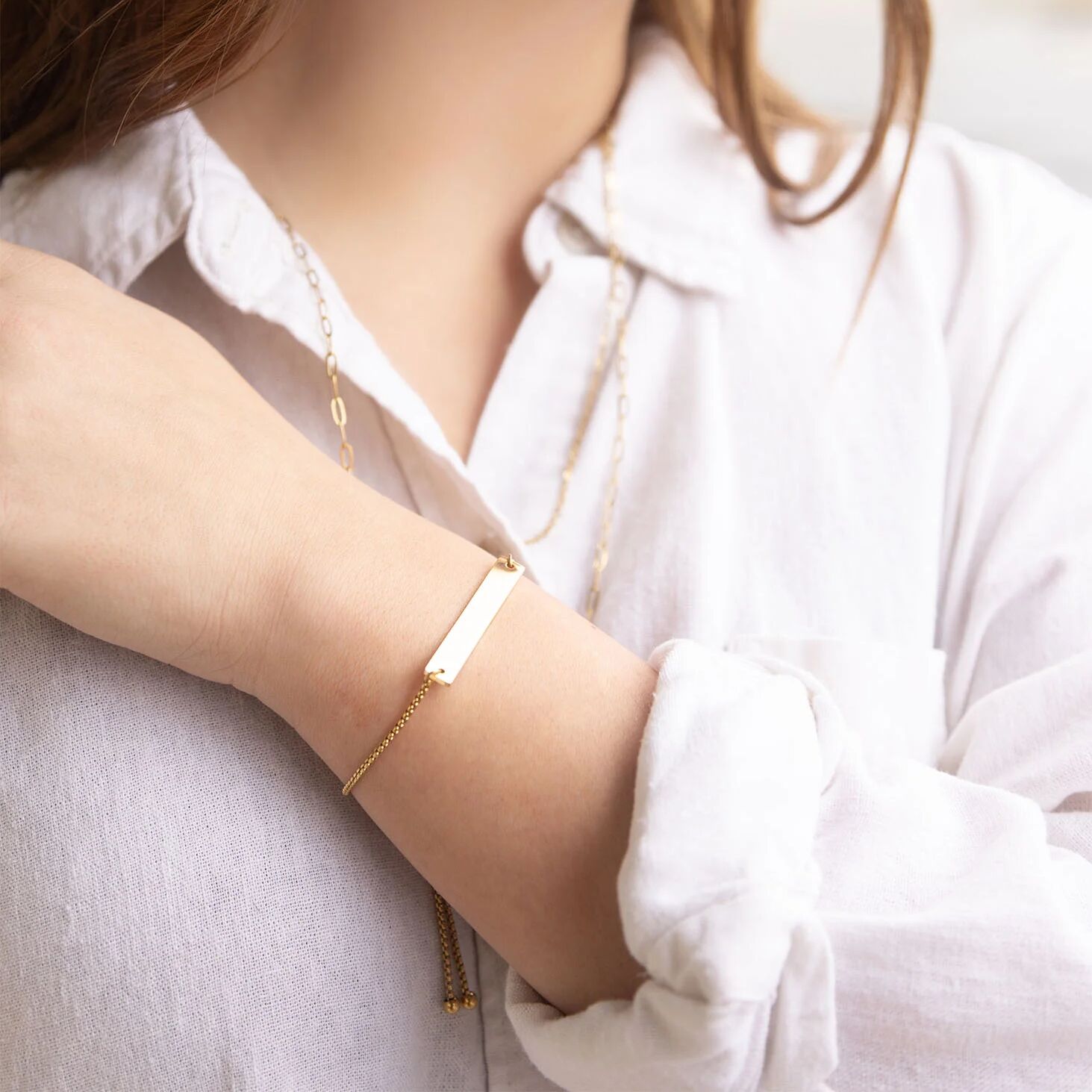 Close-up of a person wearing a gold bracelet on a light background