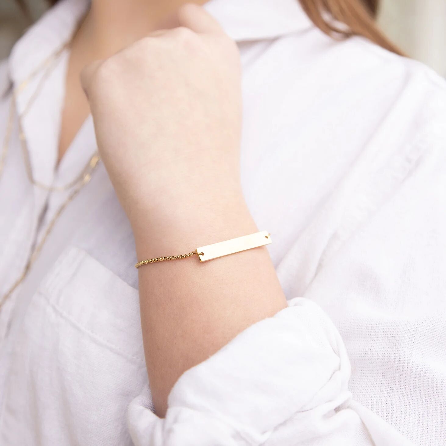 Gold bracelet on a person's wrist with a white shirt background