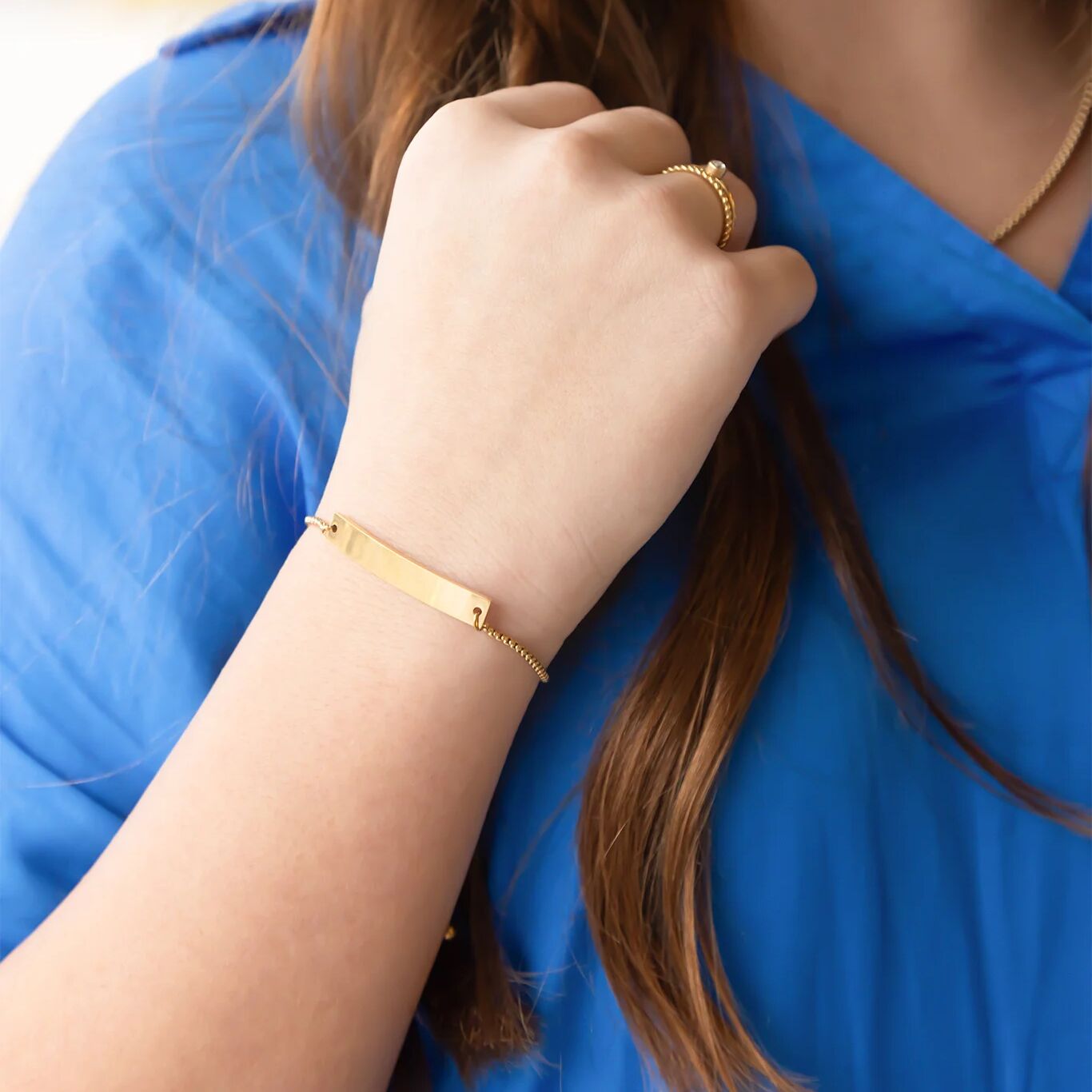 Close-up of a person wearing gold jewelry including a bracelet and ring, with a blue garment.