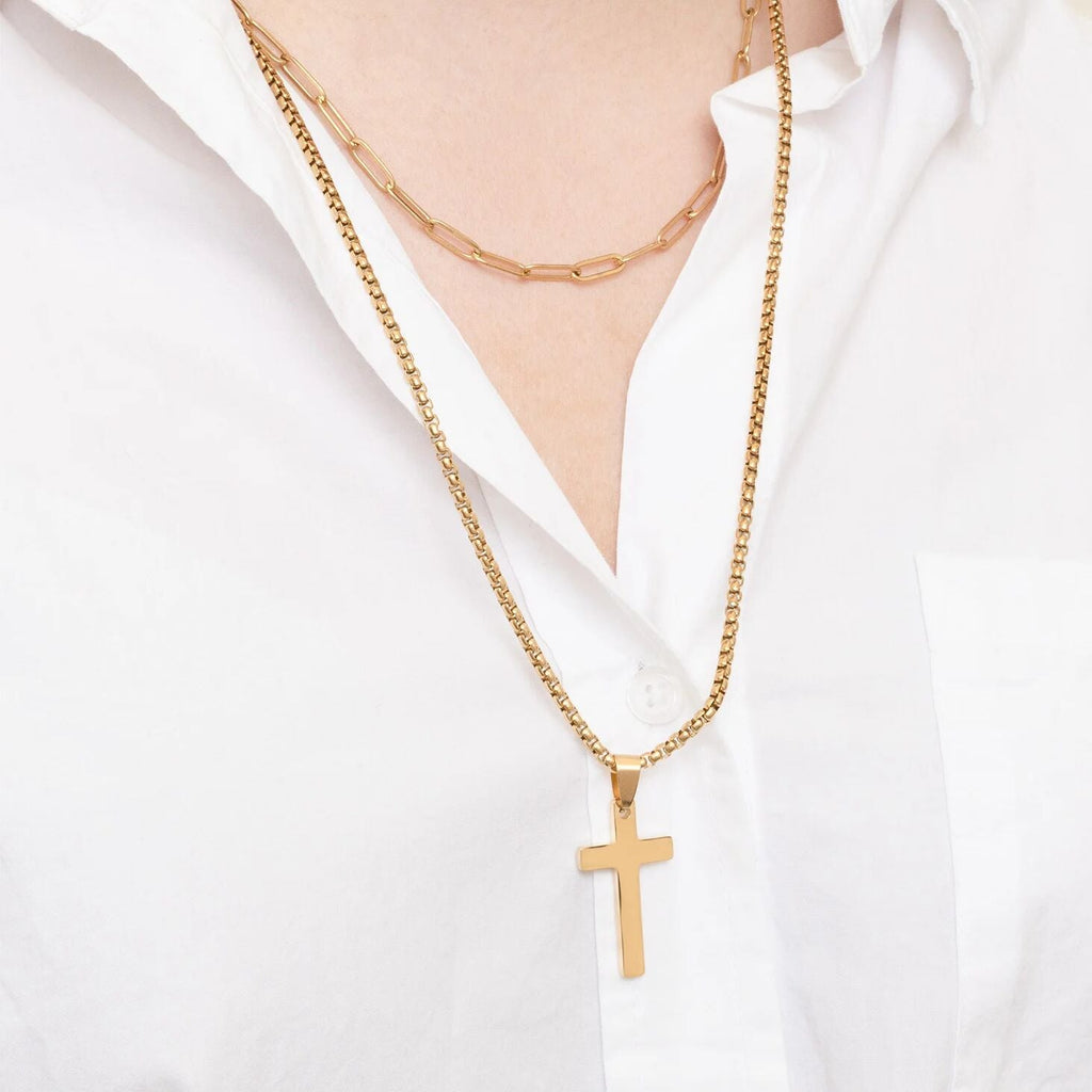 Gold cross necklace worn by a person on a white shirt background