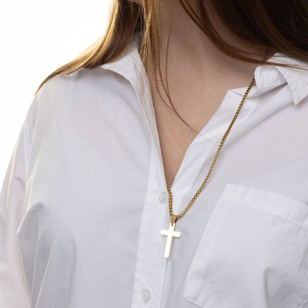 Gold necklace with a cross pendant worn by a person in a white shirt.