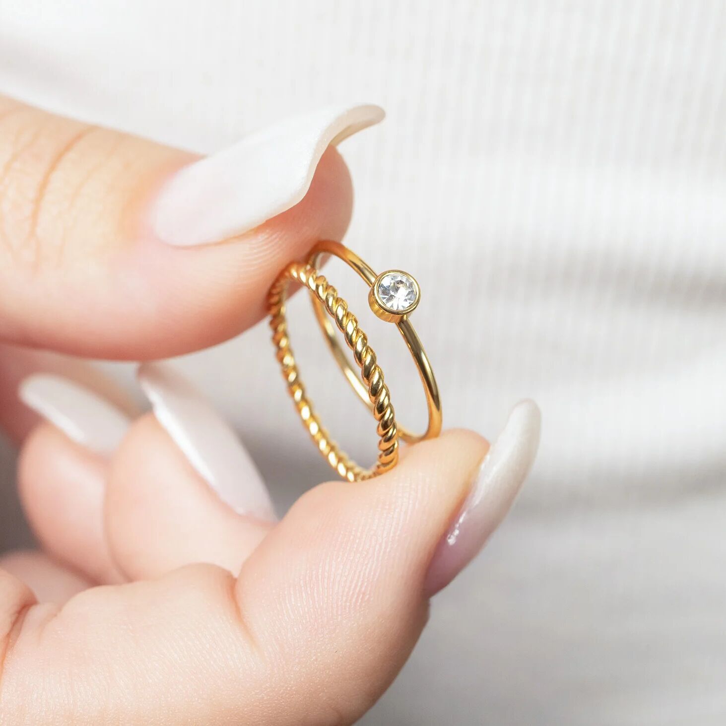Gold ring with a diamond held between fingers against a neutral background